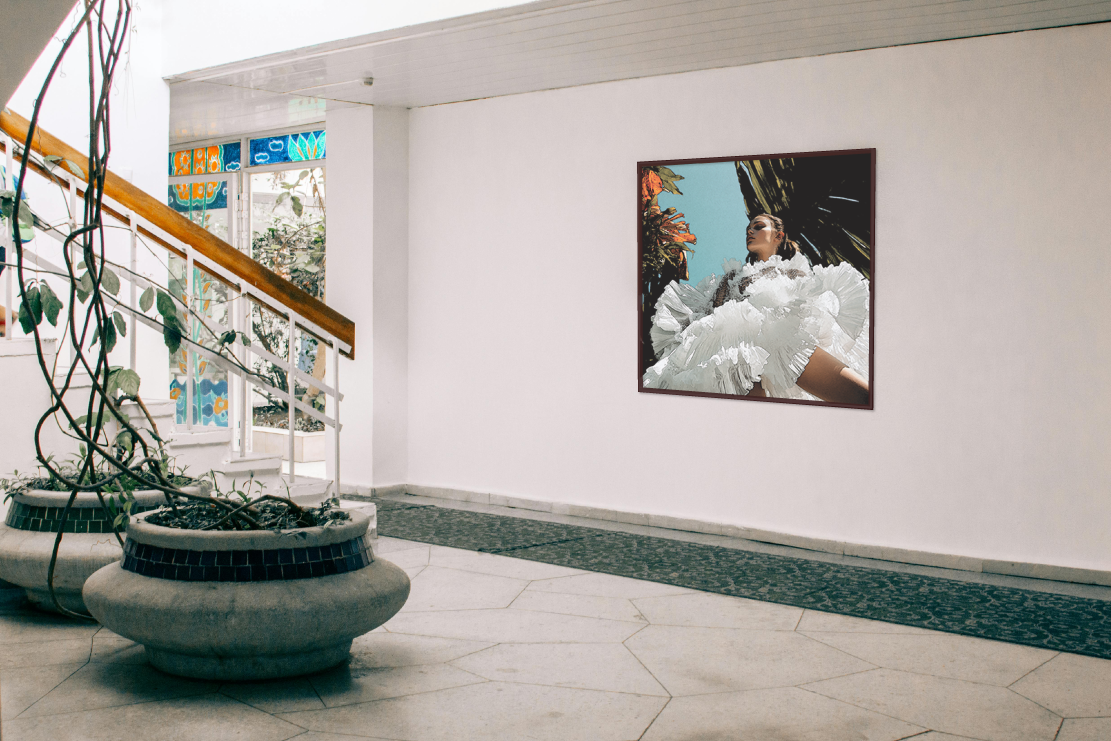 Interior hallway with staircase, plants, and a large framed photograph of a person in a white ruffled outfit on the wall, near stained glass windows.