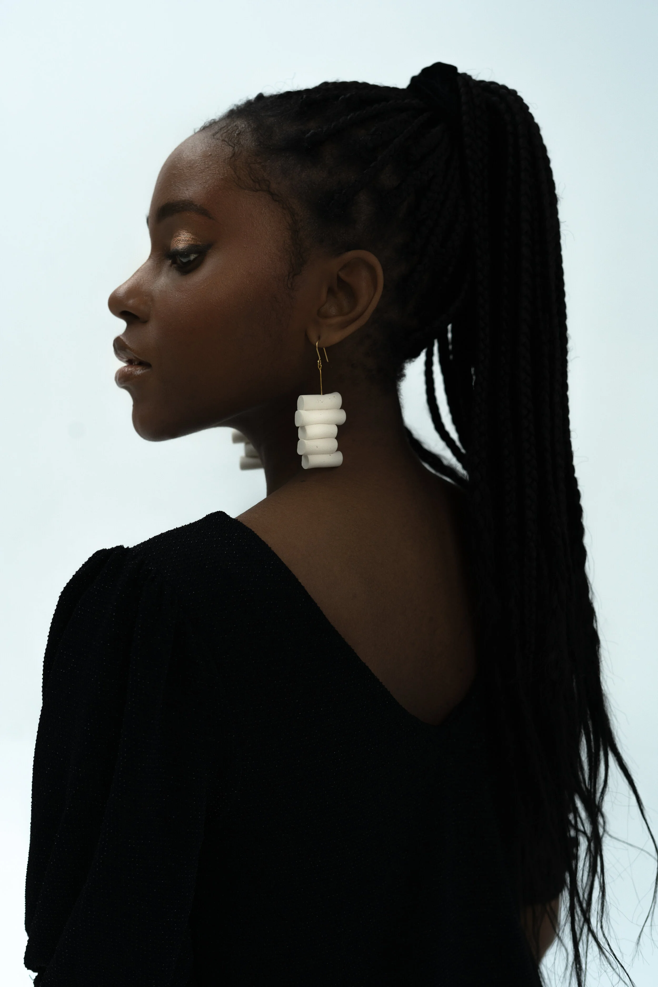 Side profile of a woman wearing long braided hair, black top, and large white earrings.