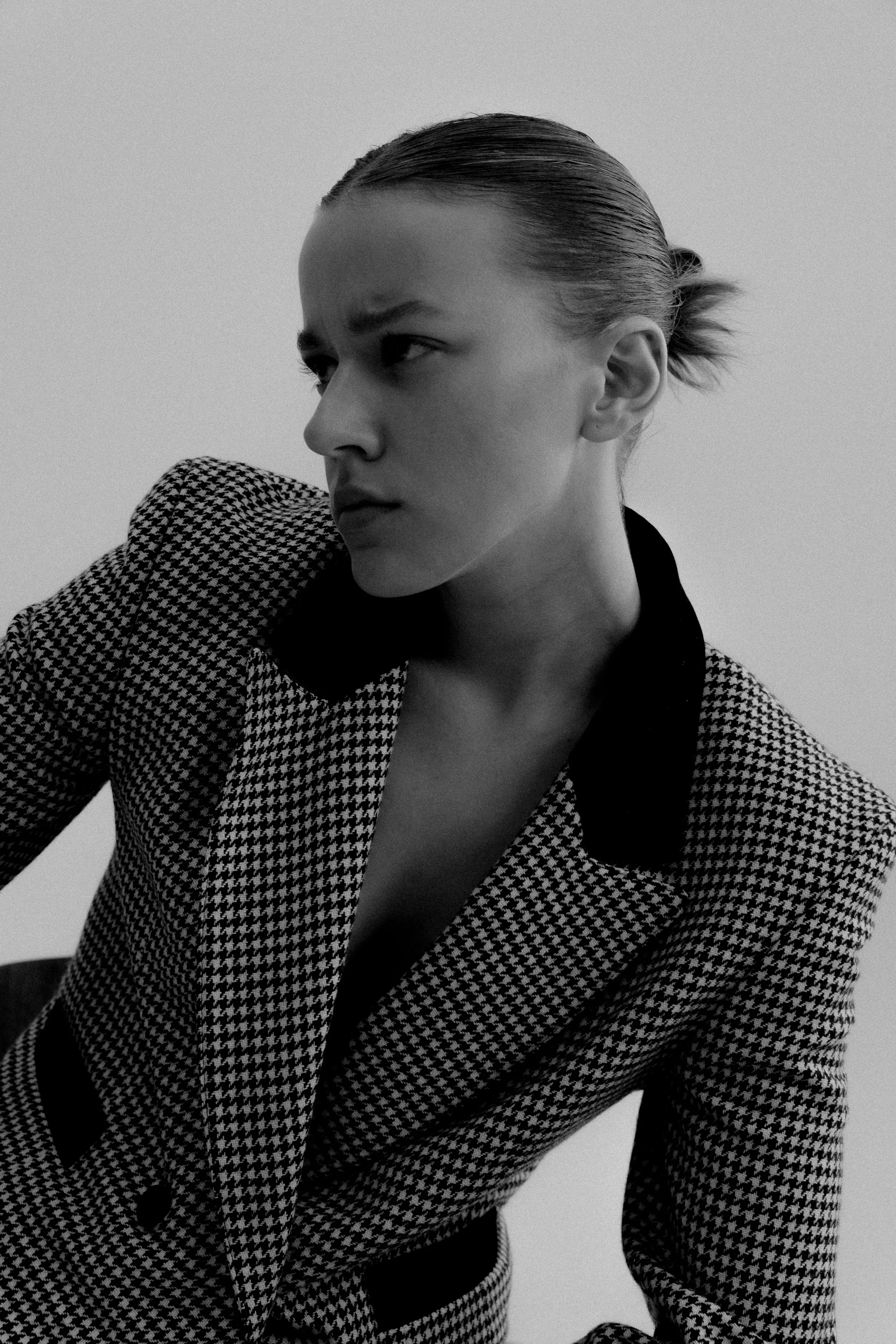 Black and white photo of a person in a houndstooth blazer with a serious expression.