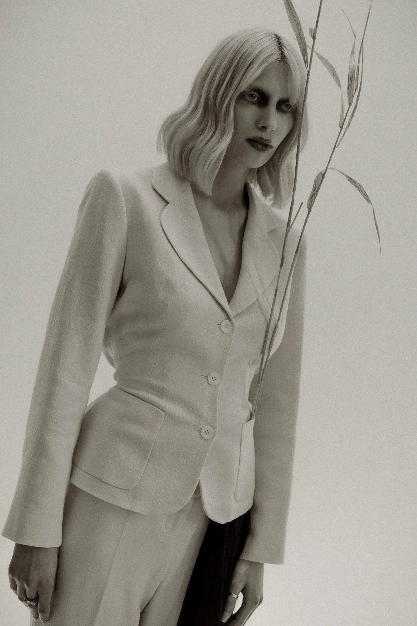 Woman in a light-colored suit holding a thin branch, monochrome image.