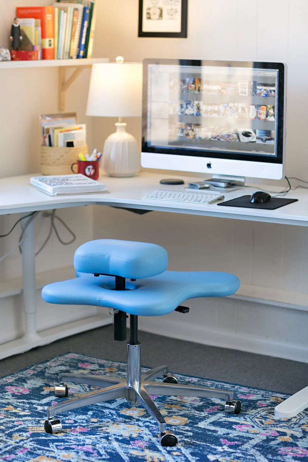 Home office desk with a computer, blue Soul Seat chair, bookshelf, lamp, and decorative items.