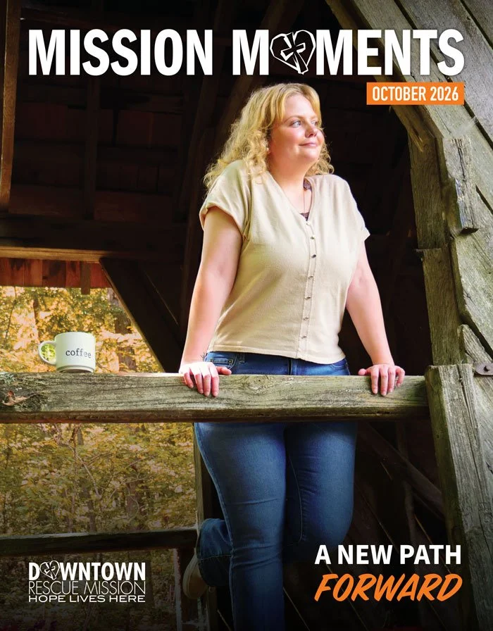 A woman with blonde hair standing on a wooden bridge or platform in a rustic setting, holding onto the railing, with a coffee mug nearby, on the cover of a magazine titled 'Mission Moments', October 2026.