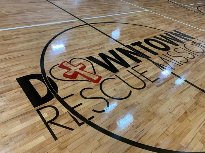 Indoor basketball court with 'Downtown Rescue Mission' logo on the floor.