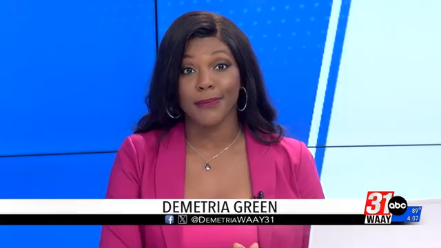 Television news anchor Demetria Green with dark hair, wearing a pink blazer and silver jewelry, sitting in front of a blue and white background.