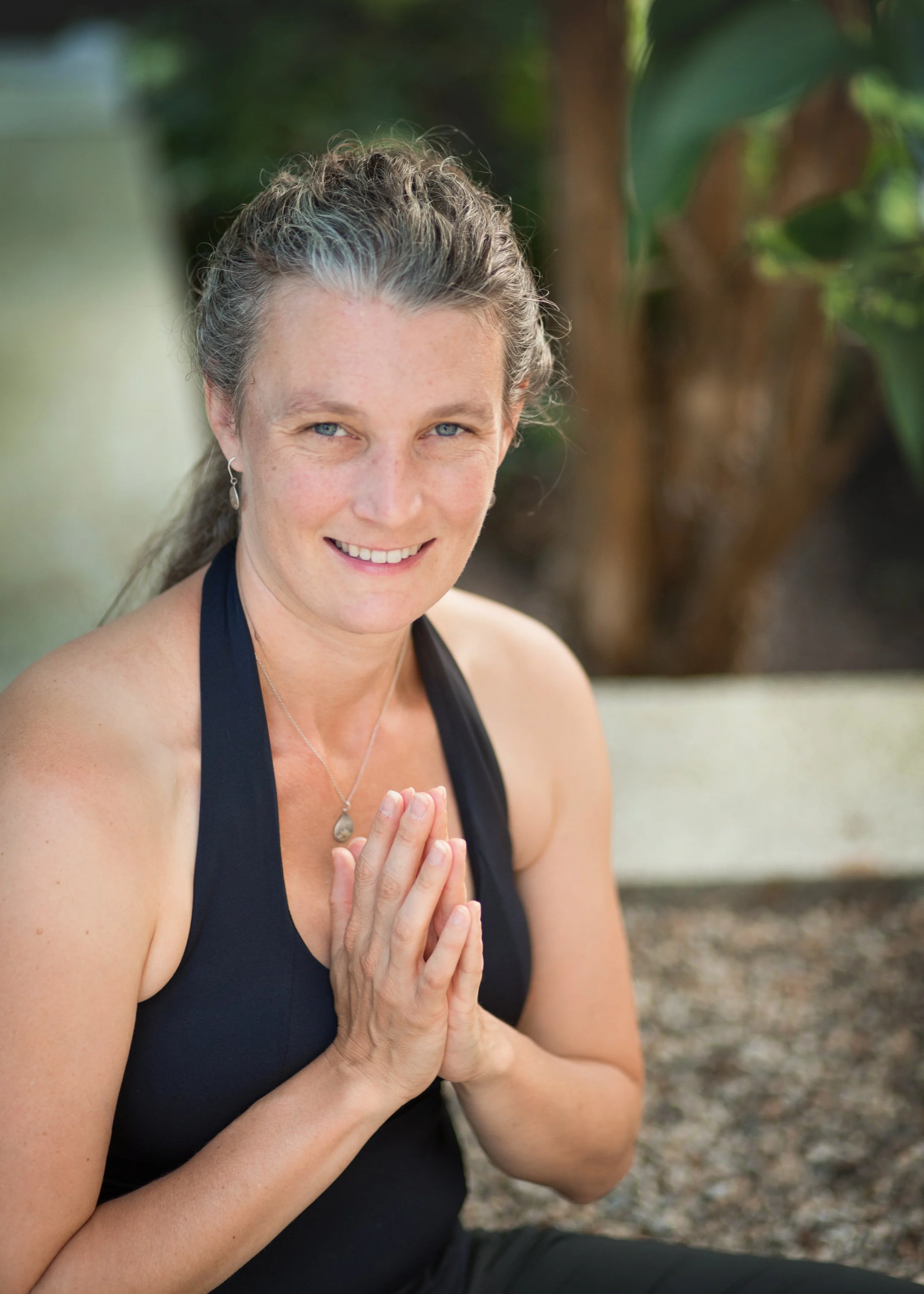Photo of Bec Conant of Om Births. She's wearing a black yoga shirt, smiling, and holding her hands in a namaste greeting.