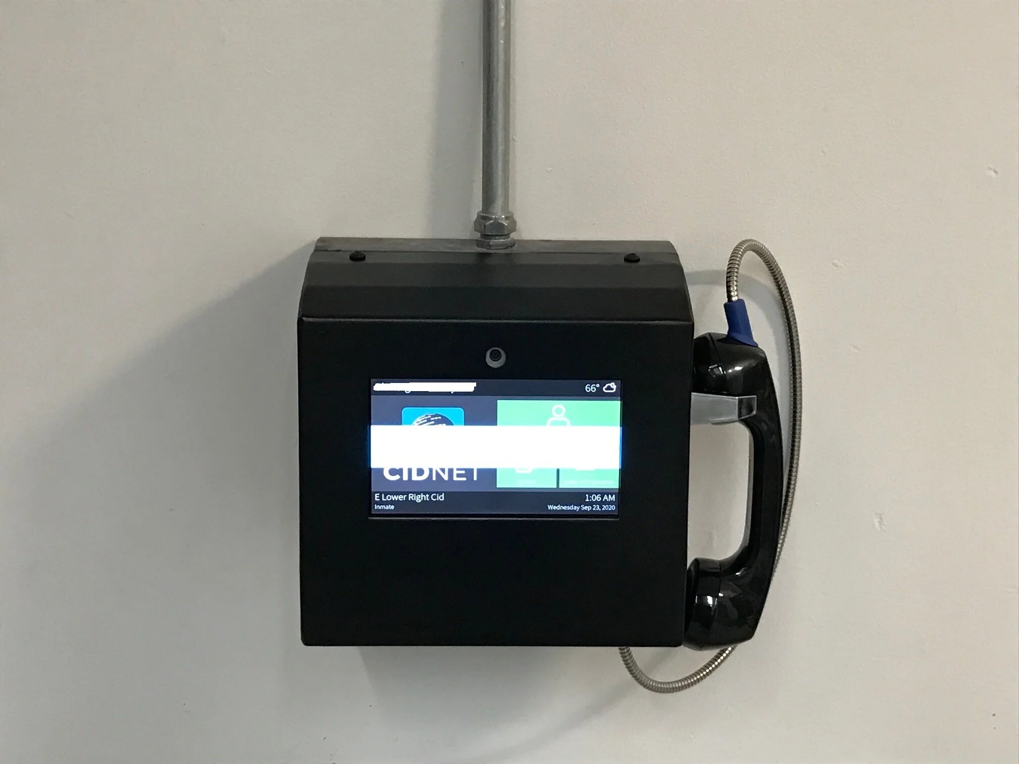 A security or monitor screen attached to a white wall showing a digital display with date, time, and information related to inmate scheduling.