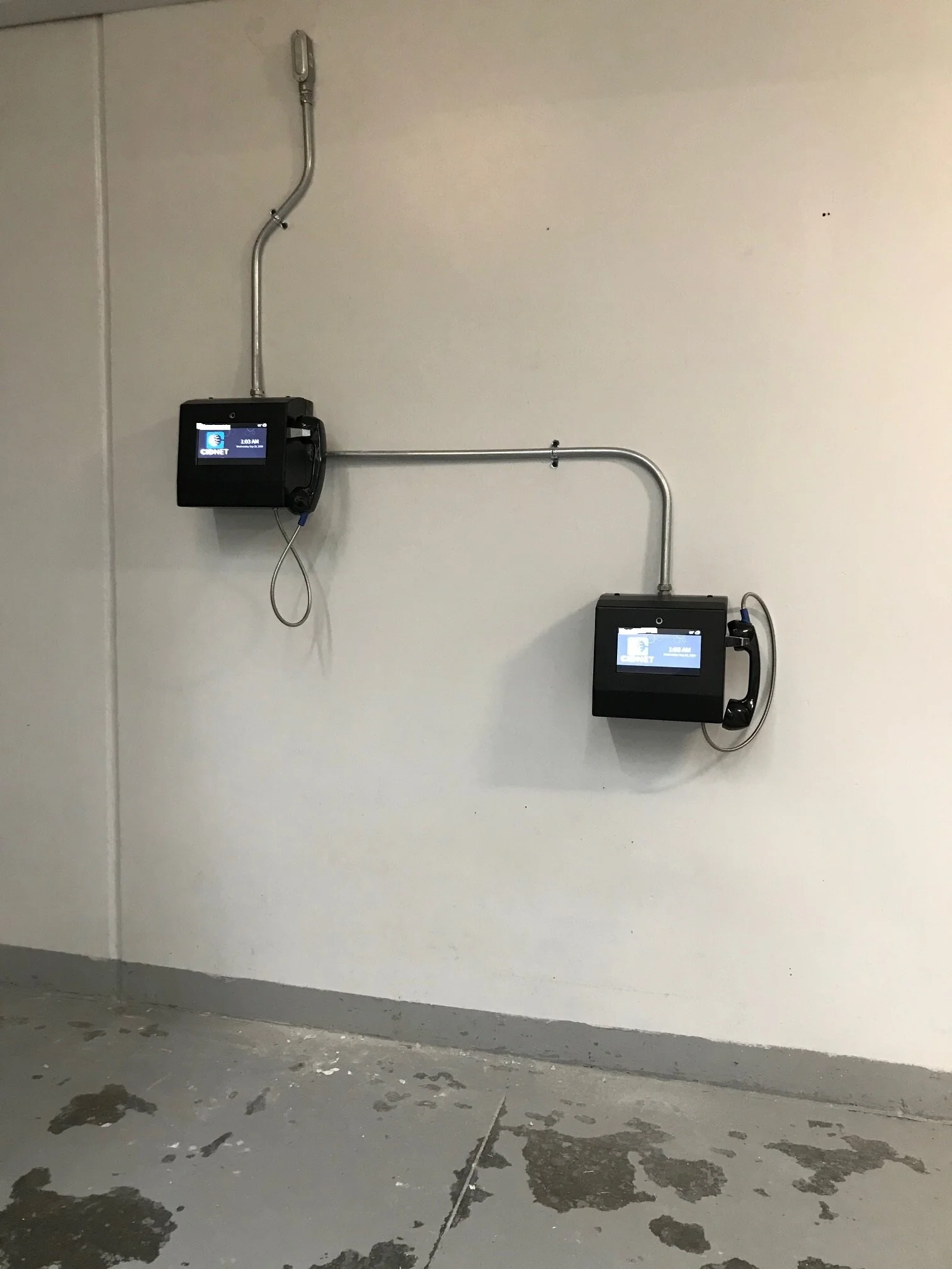Two wall-mounted phones with screens displaying 'CONNET' in an unfinished room with concrete floor and patches of water or stains.