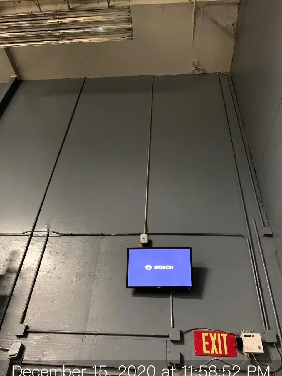 A wall with black cables, a Bosch monitor, and an illuminated red and yellow EXIT sign.