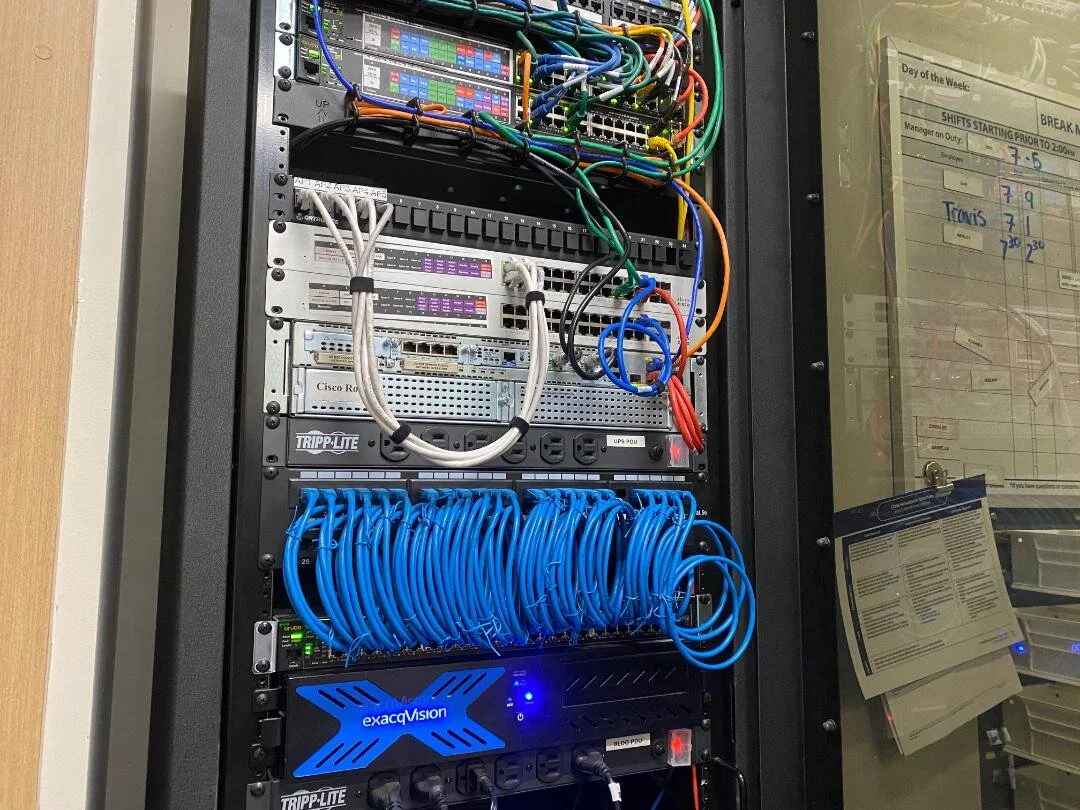 A server rack filled with networking equipment, including switches, patch panels, and numerous blue and gray Ethernet cables connected to the devices.