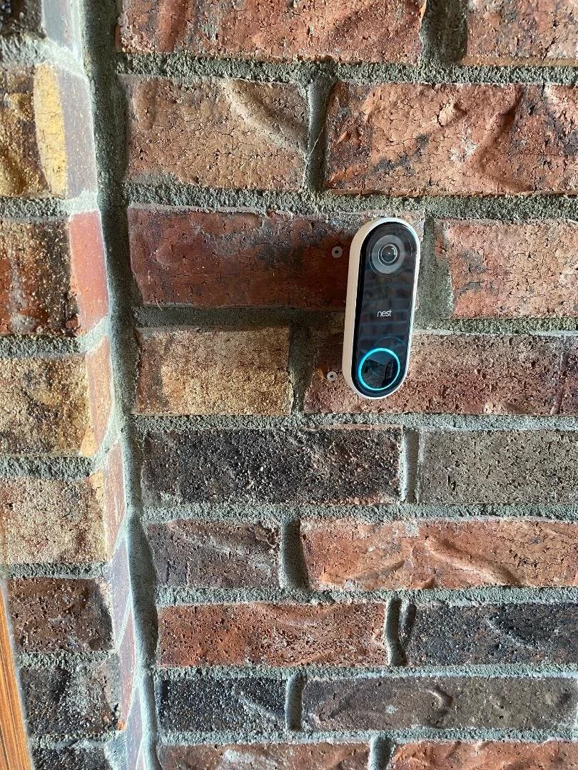 A Nest video doorbell camera mounted on a brick wall.