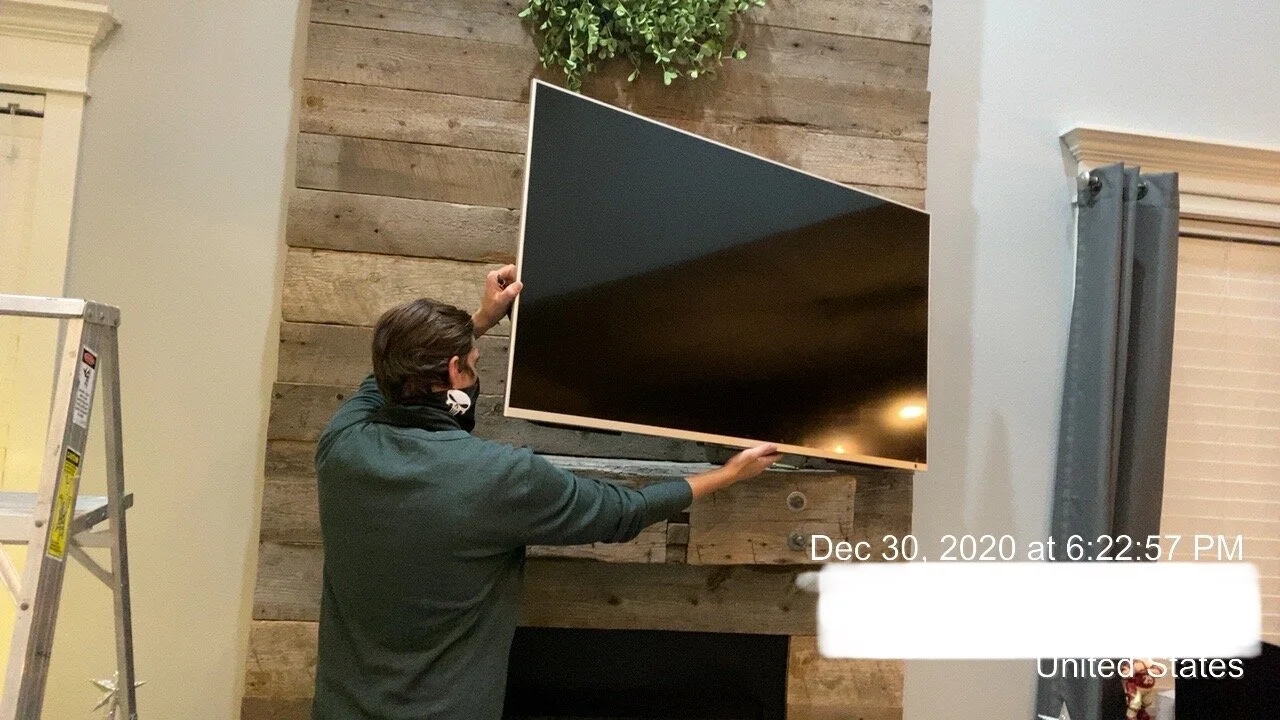 Person installing or adjusting a large flat-screen television on a wooden wall in a home or commercial setting.