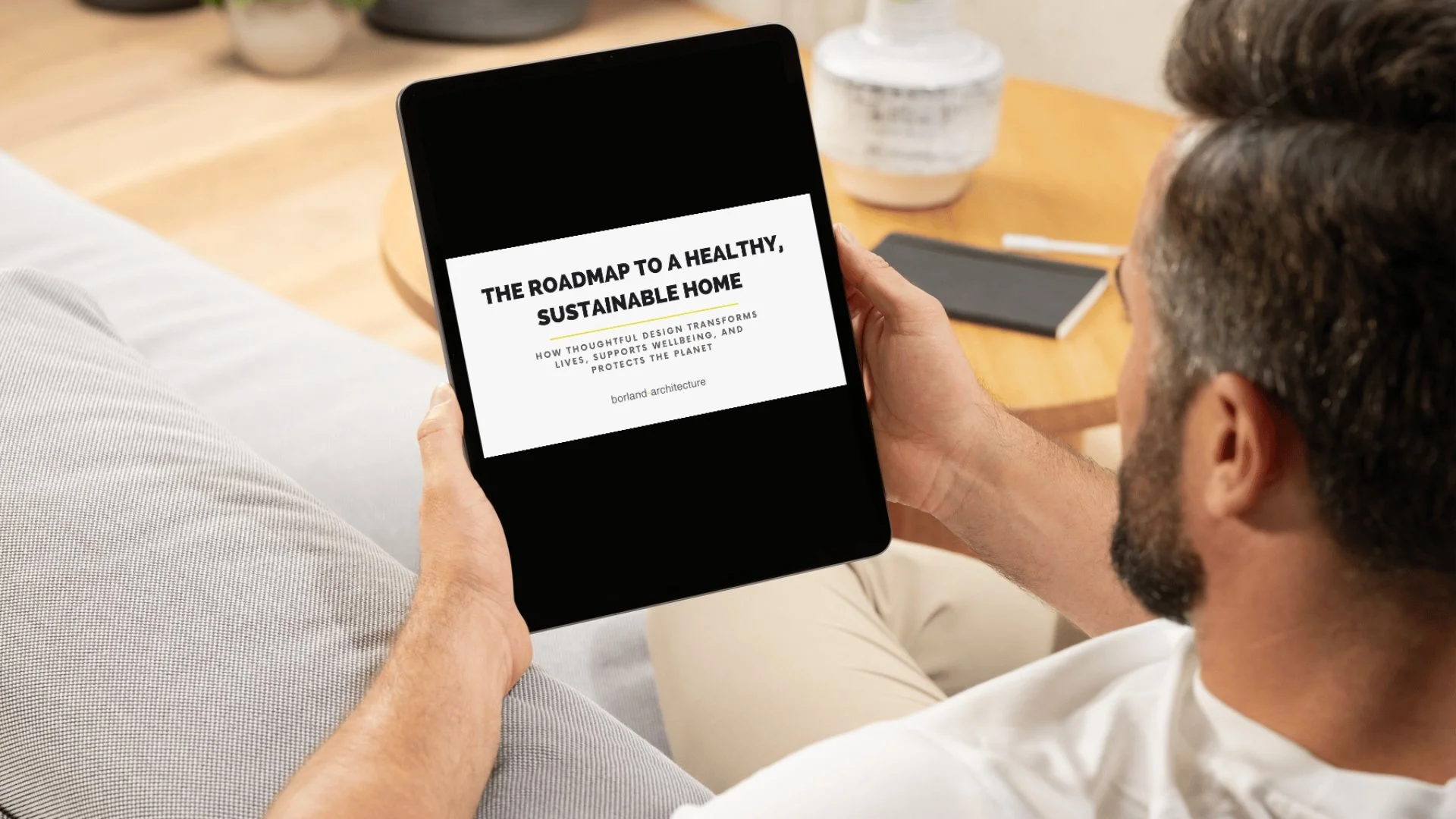 Cover of PDF download "The Roadmap To A Healthy Sustainable Home" shown on an ipad with a man sitting on a sofa