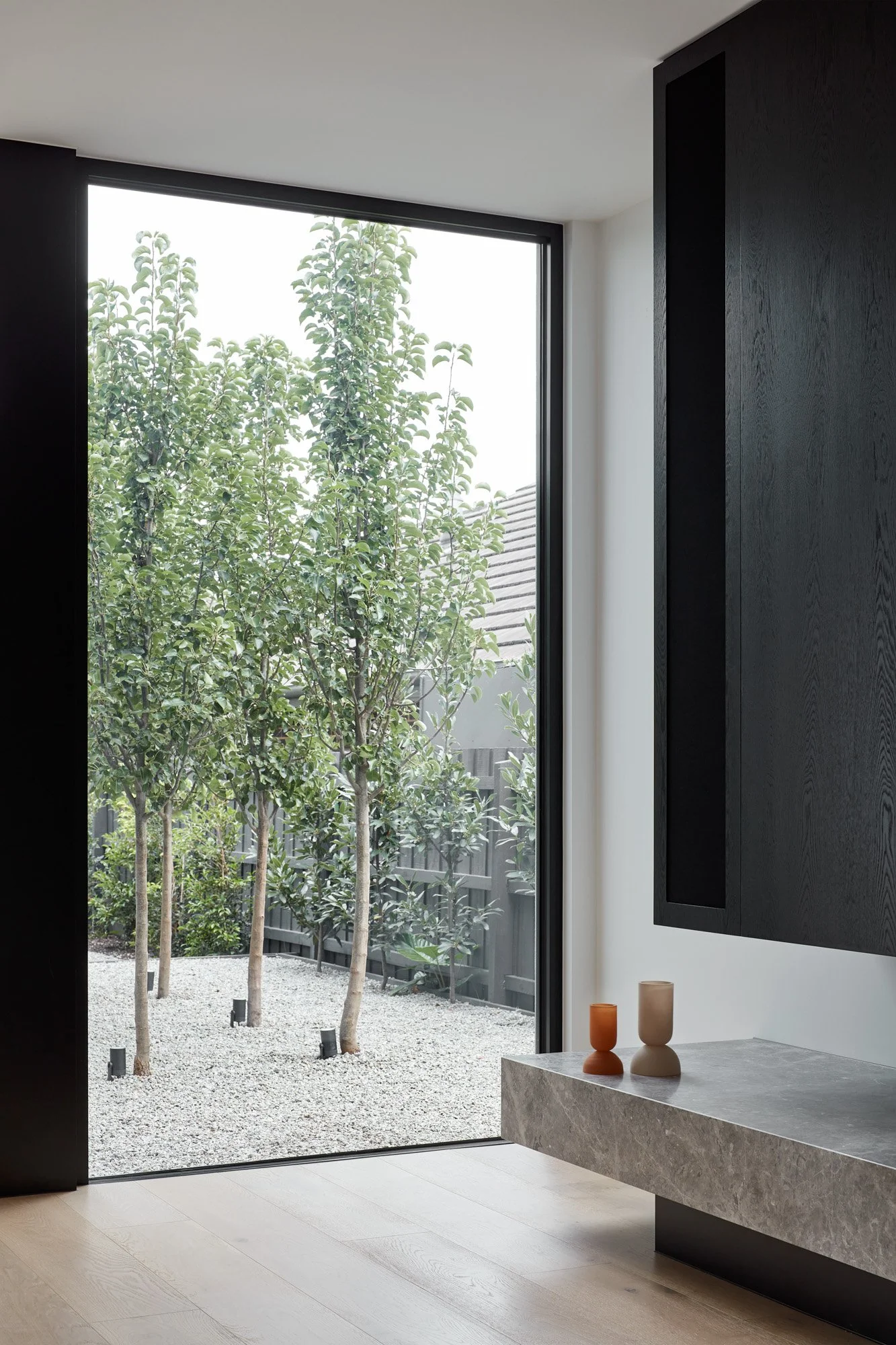 Full Height Contemporary Window overlookijg pebble courtyard with trees and a black fence