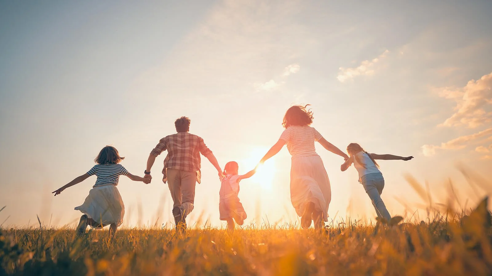 Family of four holding hand running up a grassy hill representing a family who has strengthened their connection with the help of Family Therapy in Pineville, NC.