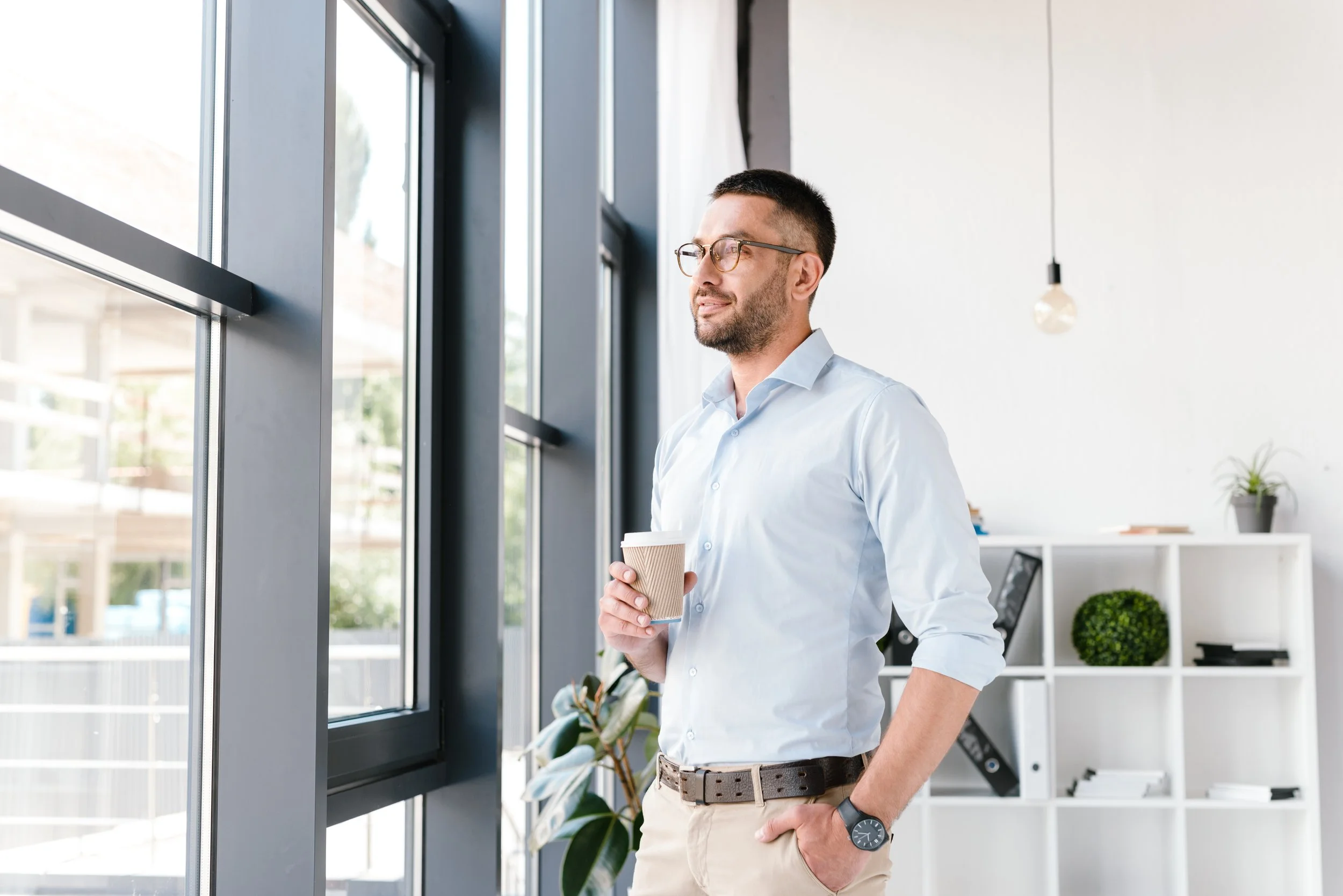 A man pausing by a window, composed and reflective — representing a surviving spouse finding steady footing while rebuilding their financial life