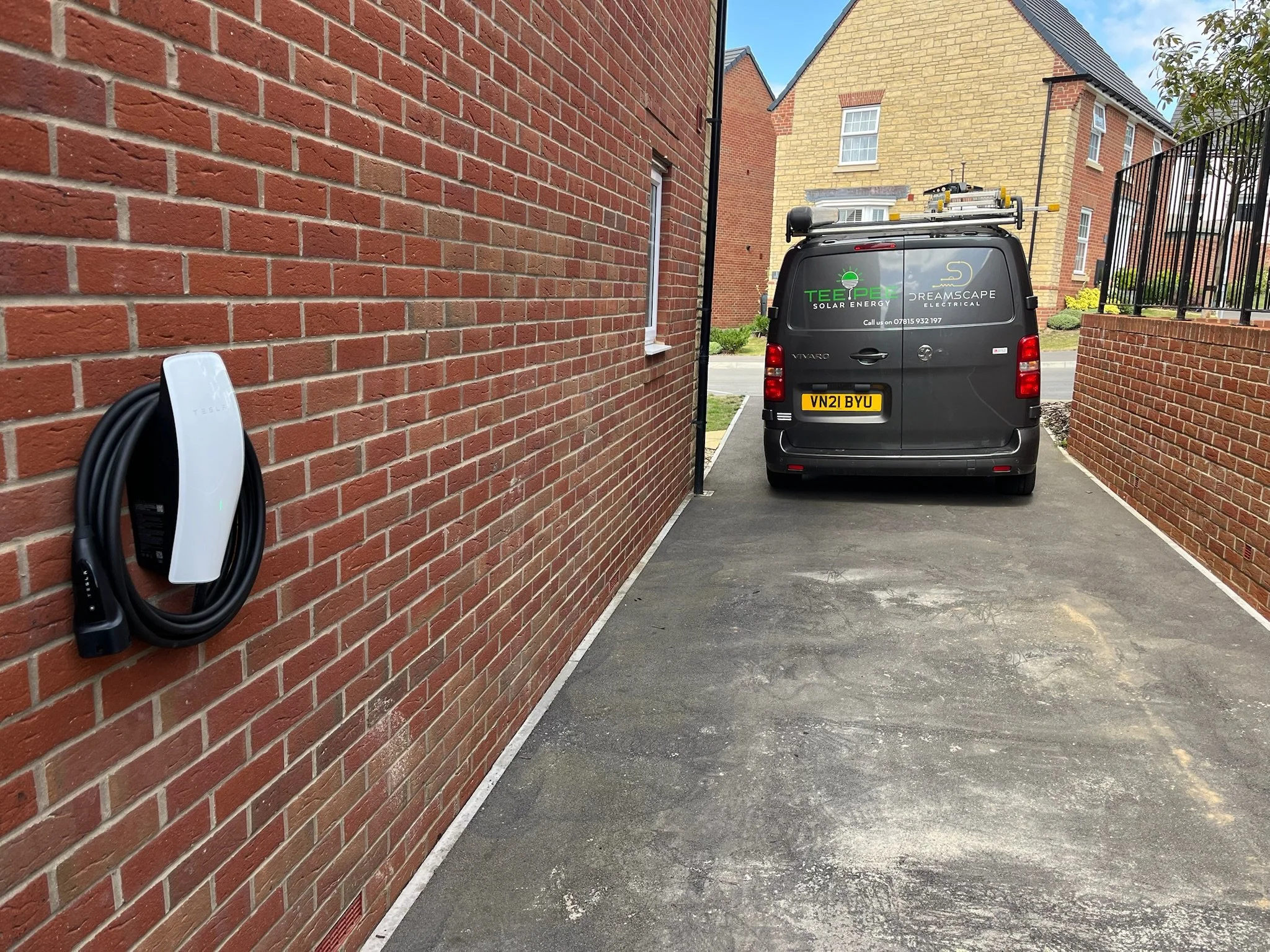 A black electric vehicle parked in a narrow driveway between red brick walls of buildings, with a solar energy company logo and contact information on the back of the vehicle.