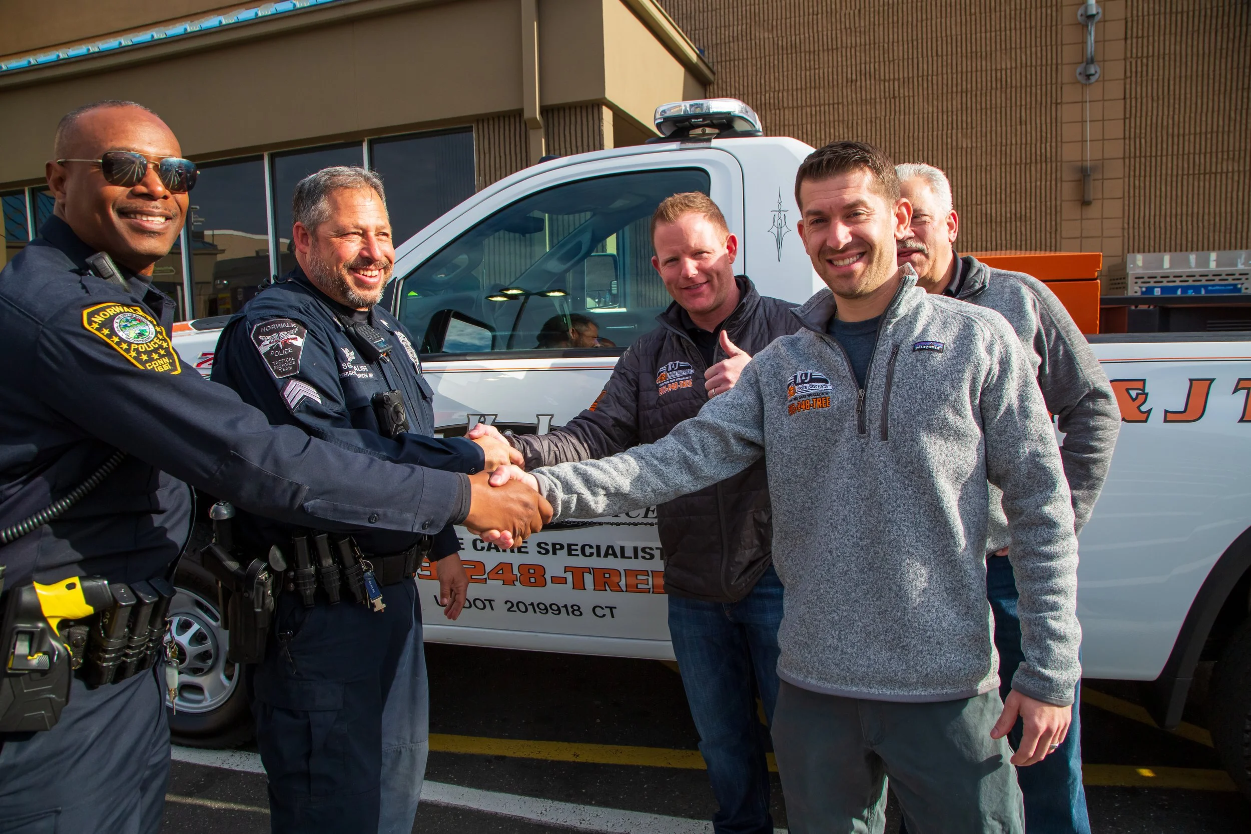 Norwalk police officers shaking hands with KJ Tree Service staff.
