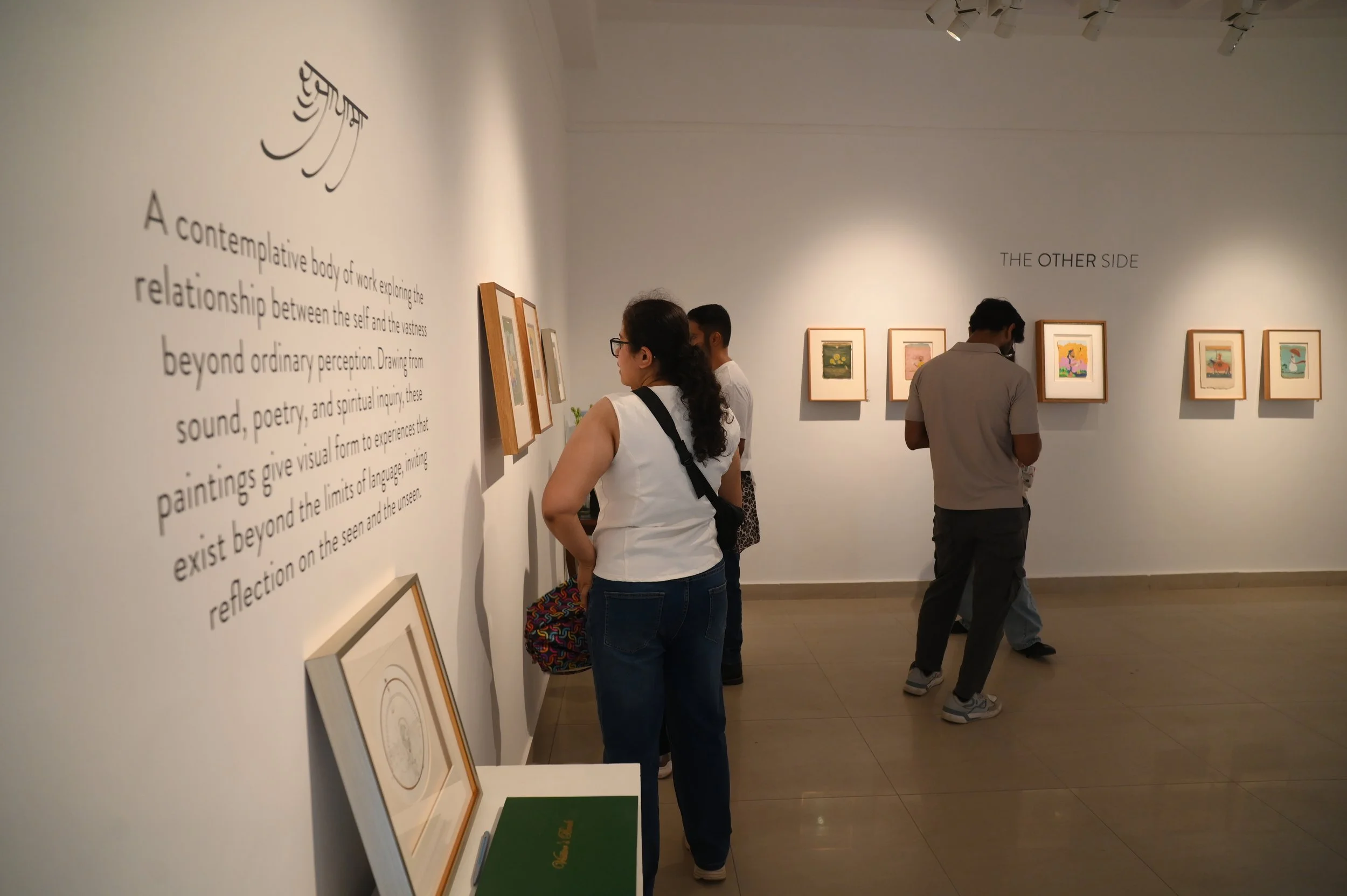 People viewing framed artwork in an art gallery with white walls, along with written descriptive text on the wall.