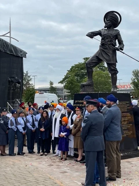 Sikh community standing next to bronze sculpture of sikh soldier drawing a sword
