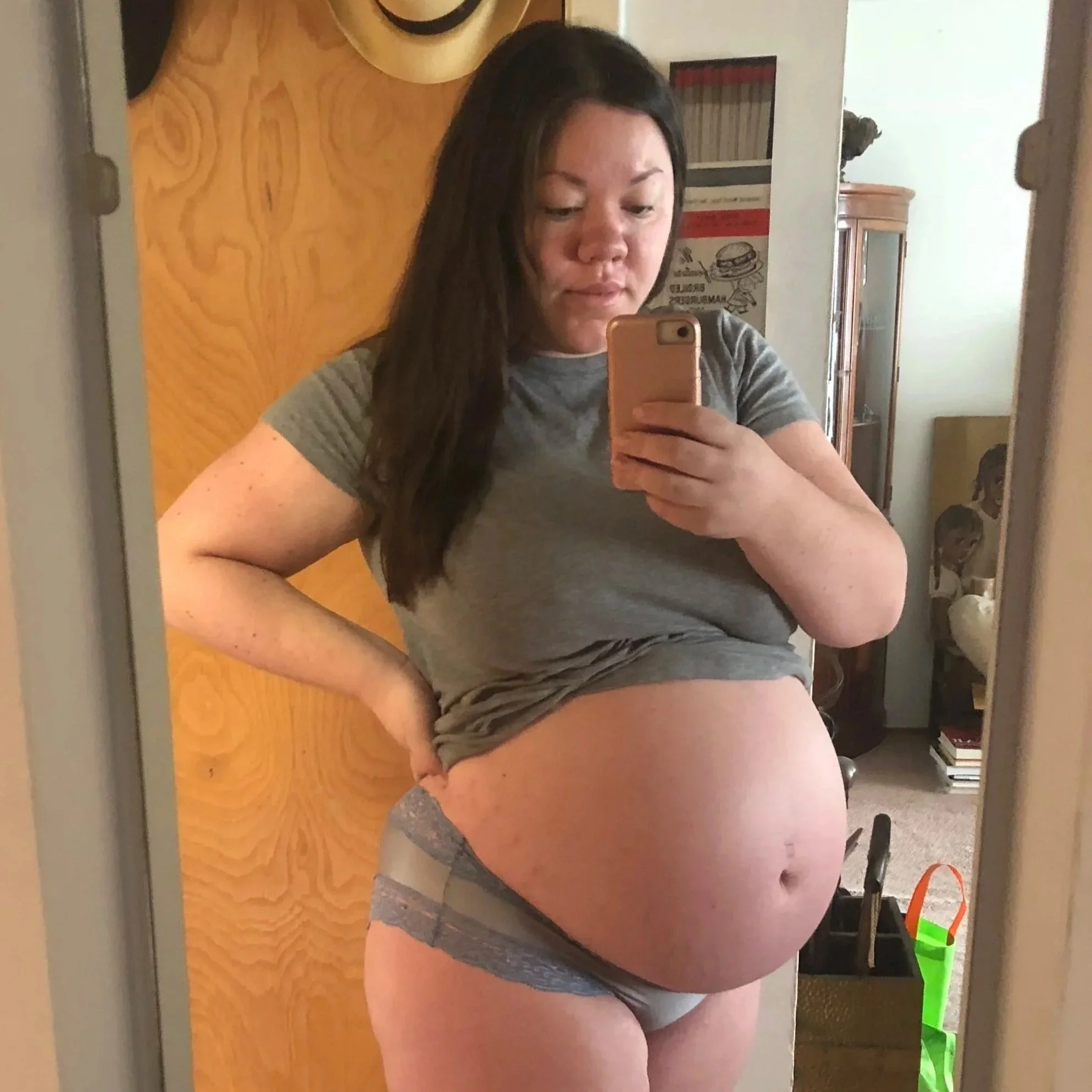 a photo of Siobhan, a fair skinned mixed filipino femme with long dark hair at 9 months pregnant. Her belly is exposed as she takes a photo with her phone in the mirror.