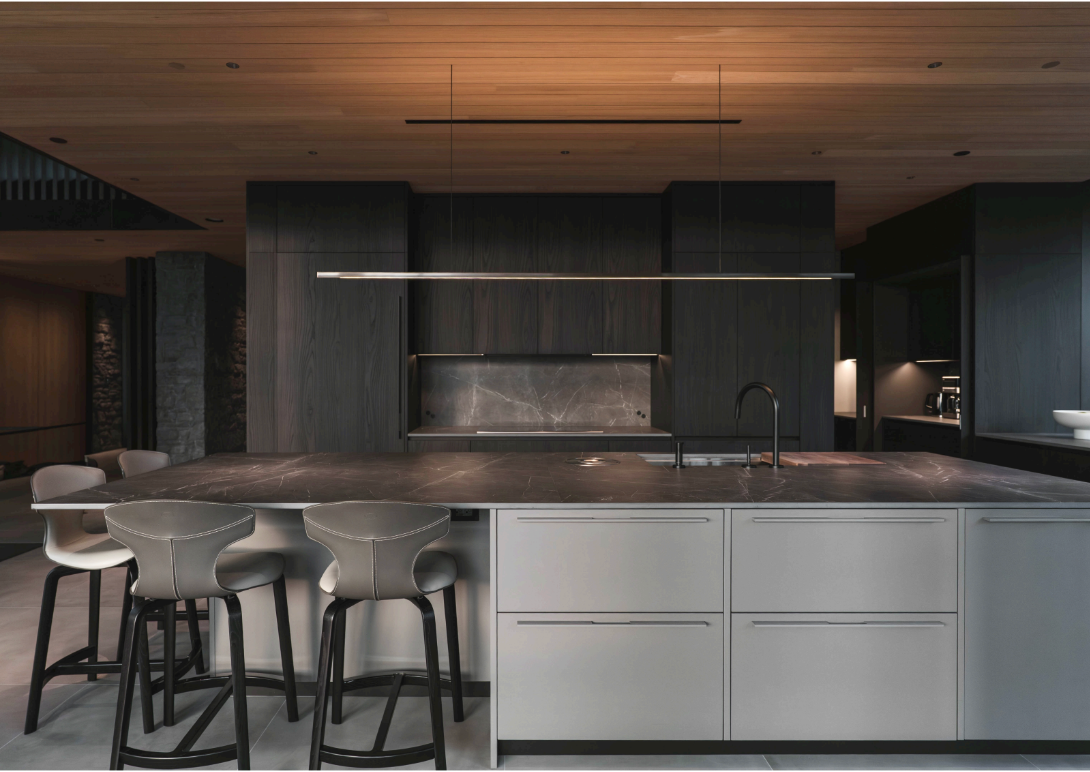 Modern kitchen with a dark marble island, black cabinets, and wooden ceiling, featuring bar stools.