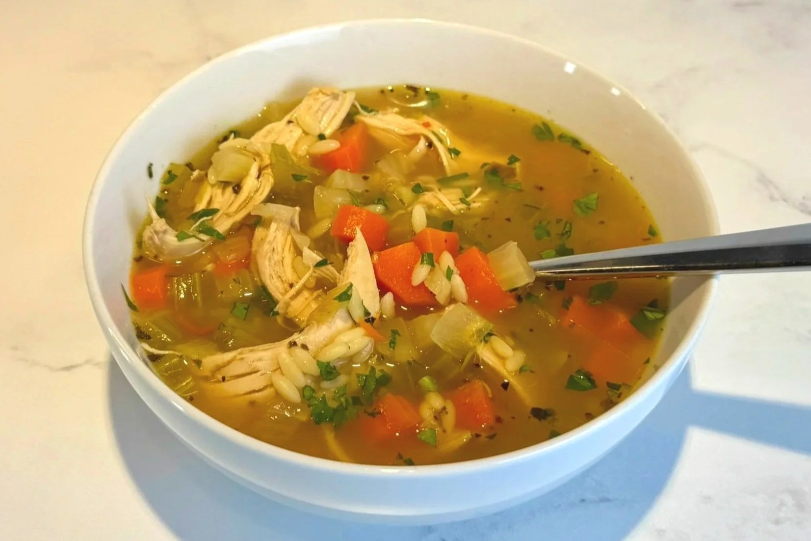 A bowl of fresh and chunky Lemon Chicken Orzo Soup sitting on a counter ready to enjoy!
