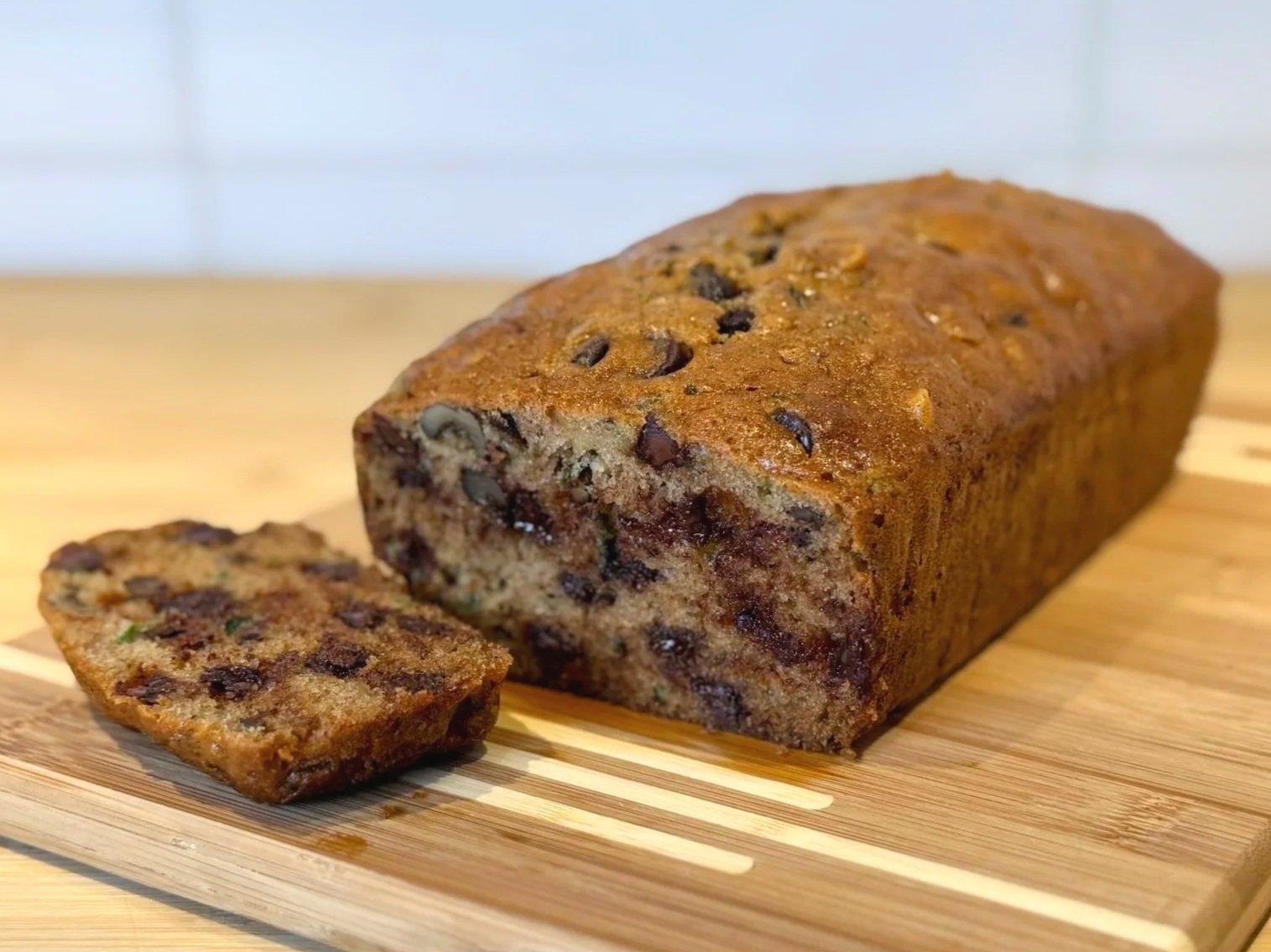 A sliced loaf of Chocolate Chip Zucchini Bread sitting on a cutting board.