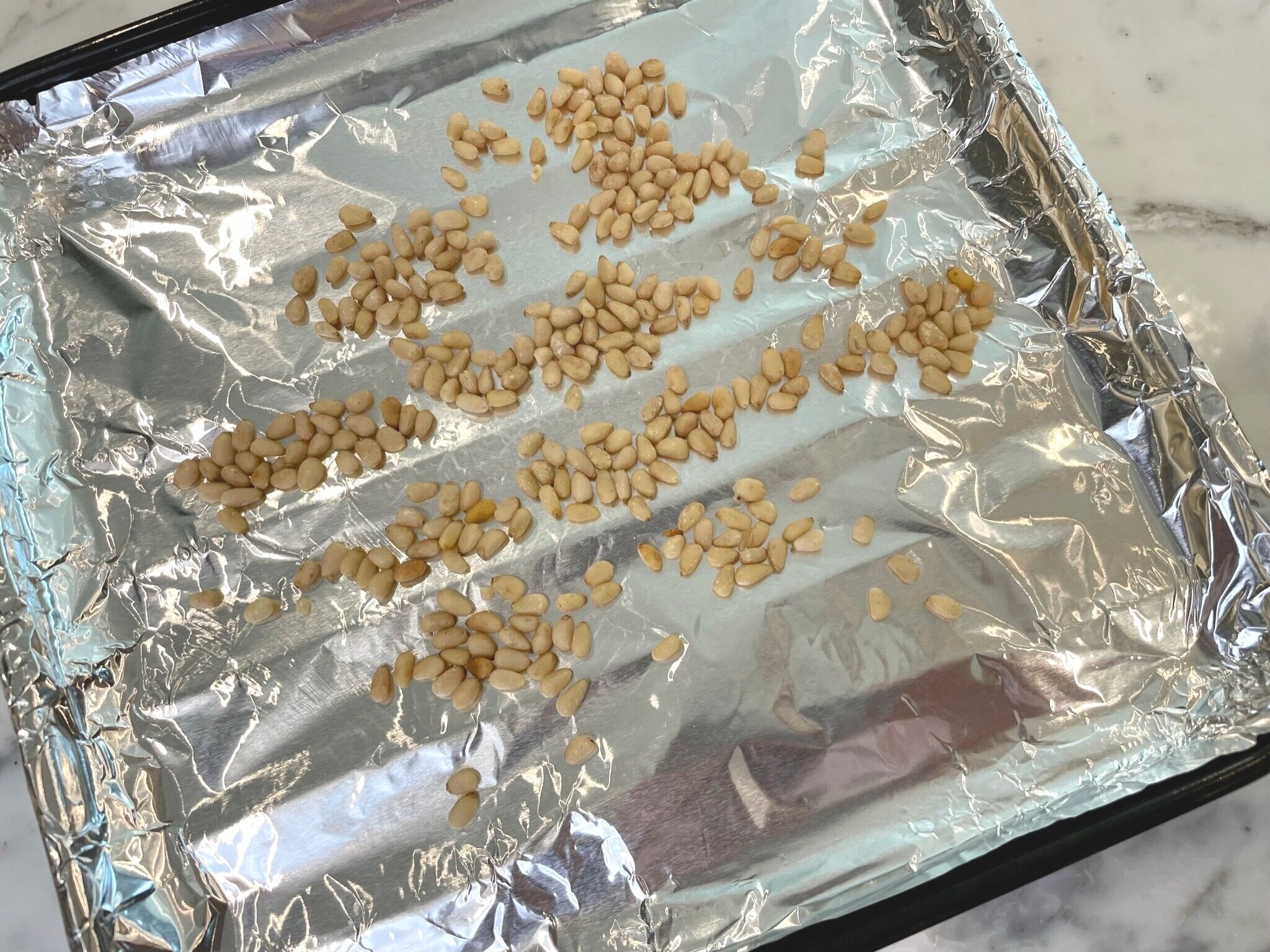 Spread pine nuts on baking pan.