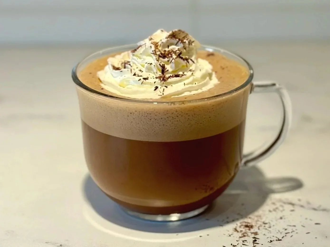 A glass mug of Protein Peppermint Mocha Latte topped with whipped cream and chocolate shavings.