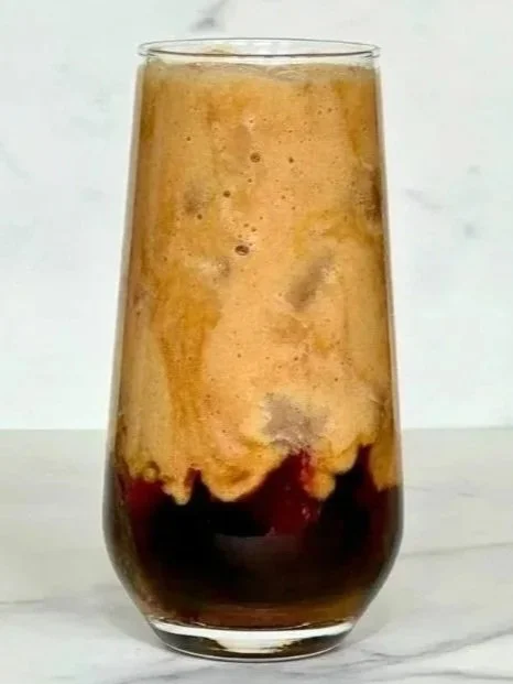 A tall glass of iced Healthy Banana Milk Latte sitting on a marble countertop.