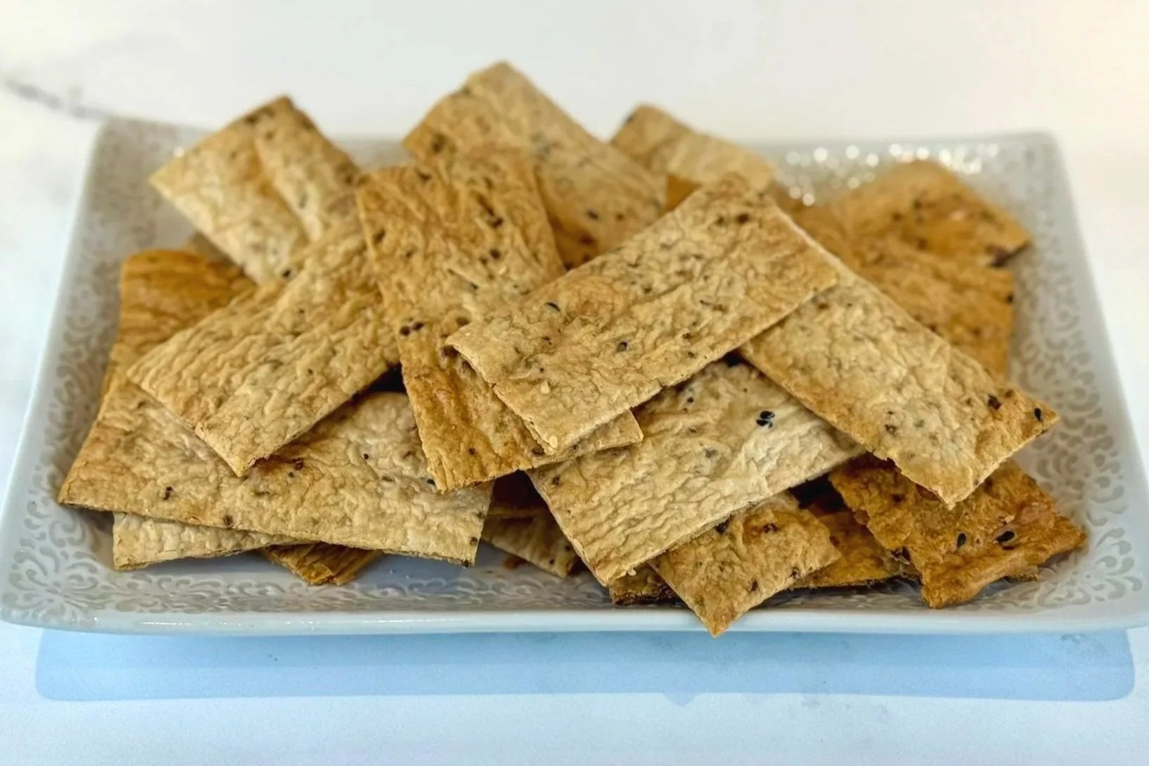 A white rectangular platter filled with a pile of Everything Bagel Sourdough Discard Crackers.