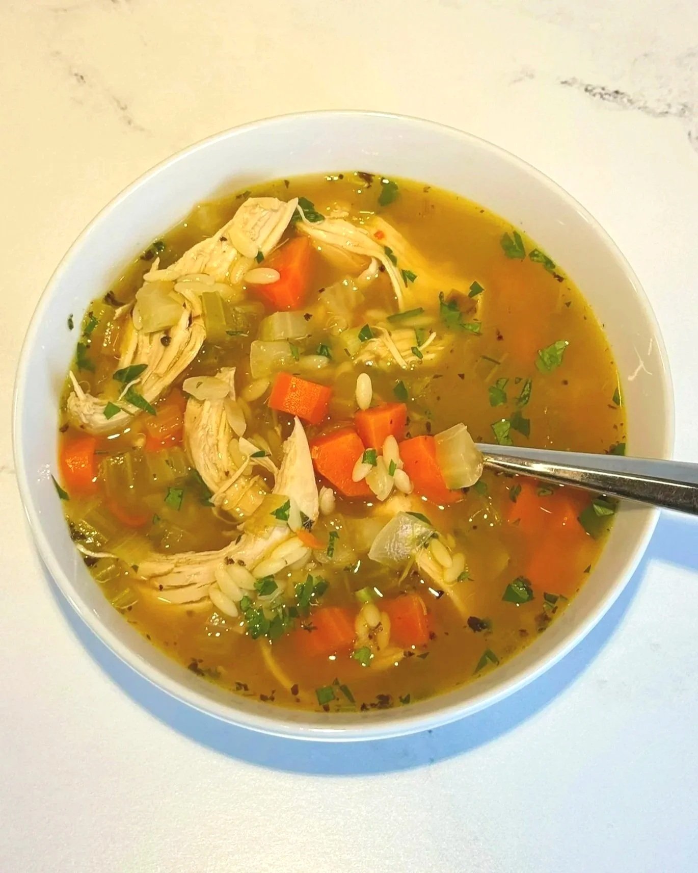 A bowl of fresh and chunky Lemon Chicken Orzo Soup sitting on a counter ready to enjoy!