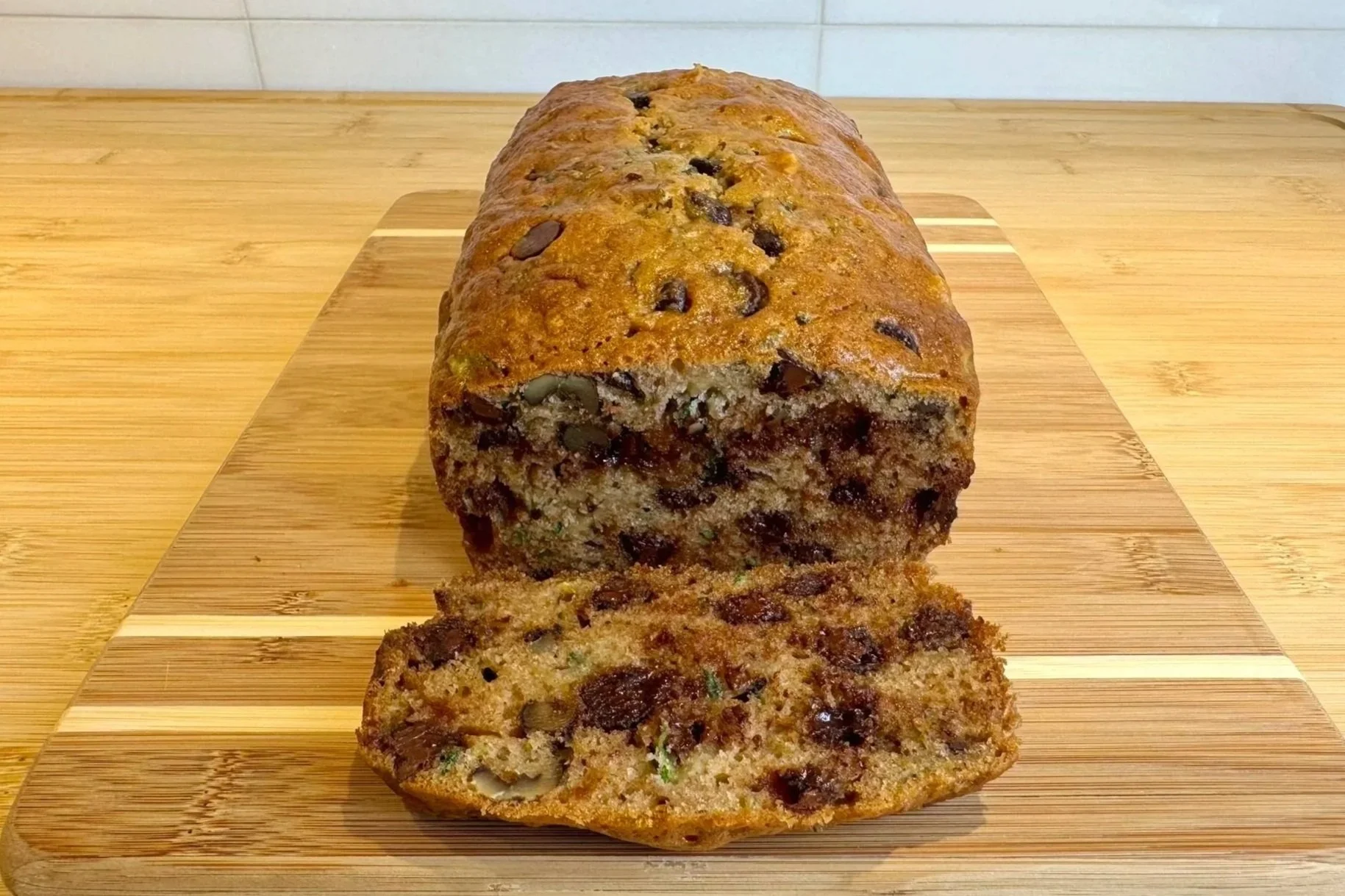 A loaf of Chocolate Chip Zucchini Bread that is sliced on a cutting board.