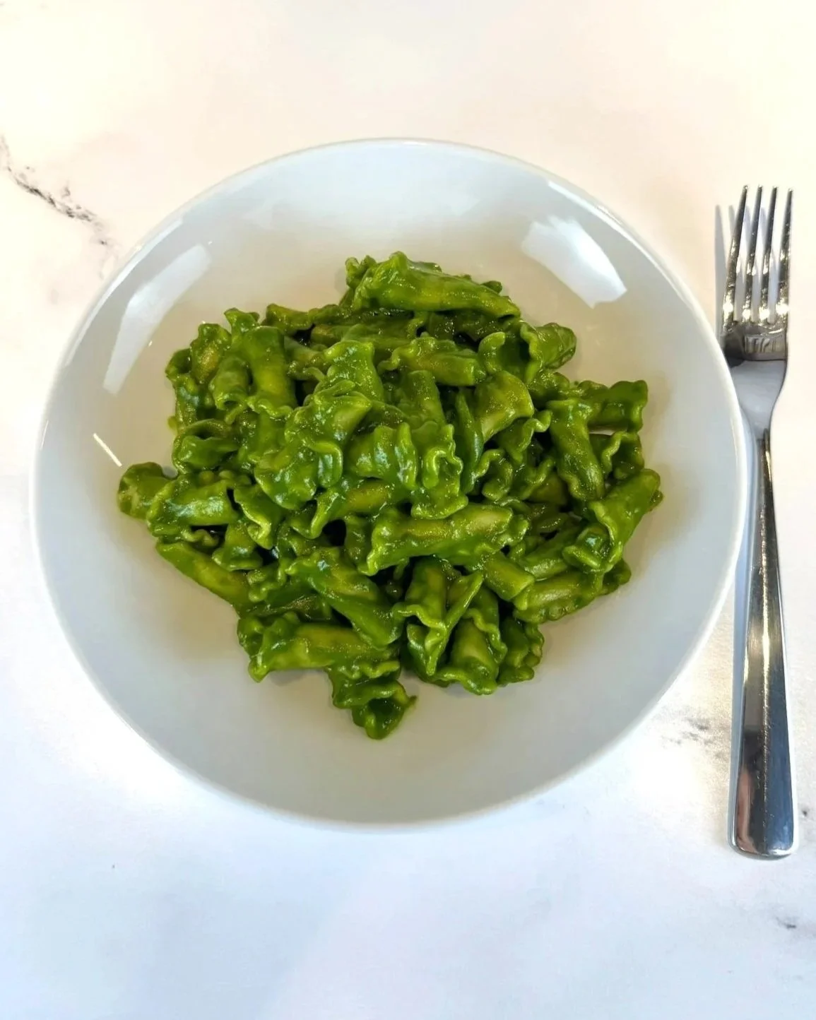 A bowl of Garlicky Kale Pasta (also known as Shrek Pasta) with a fork on the counter.