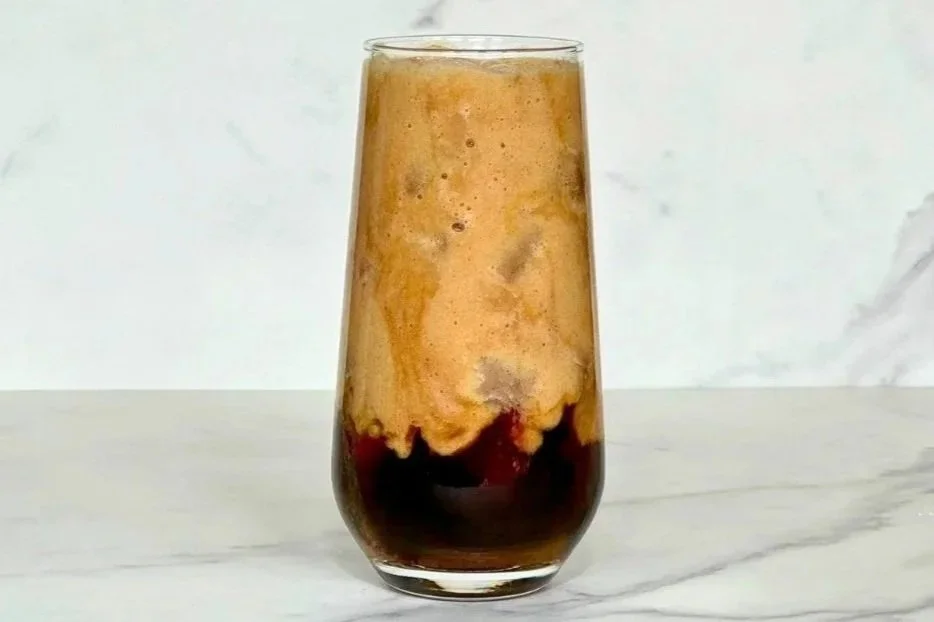 A tall glass of iced Healthy Banana Milk Latte sitting on a marble countertop.