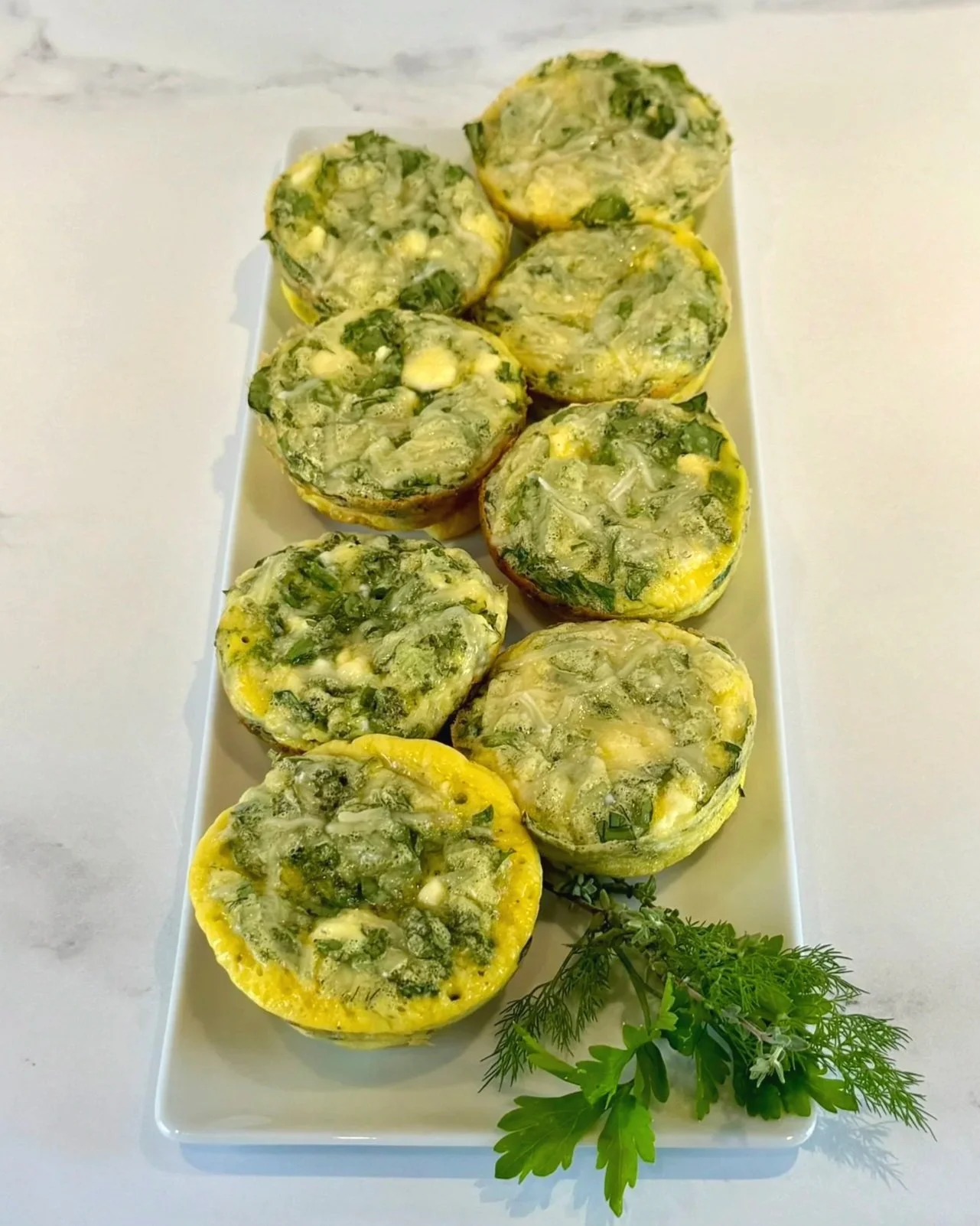 A rectangular serving platter filled with 8 Spinach Feta Egg Bites with a garnish of fresh herbs.