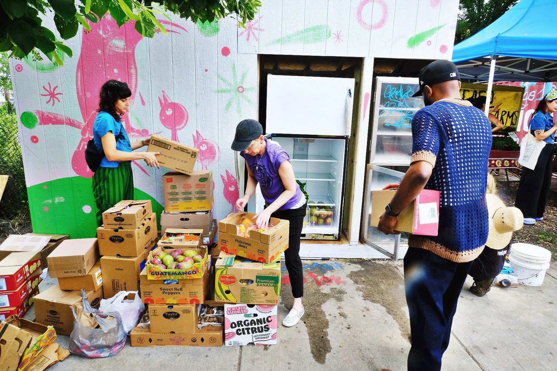 volunteers clean and stock a colorfully painted community fridge