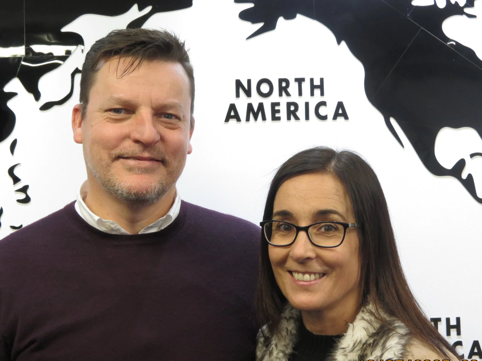 A man and a woman smiling in front of a North America map background.