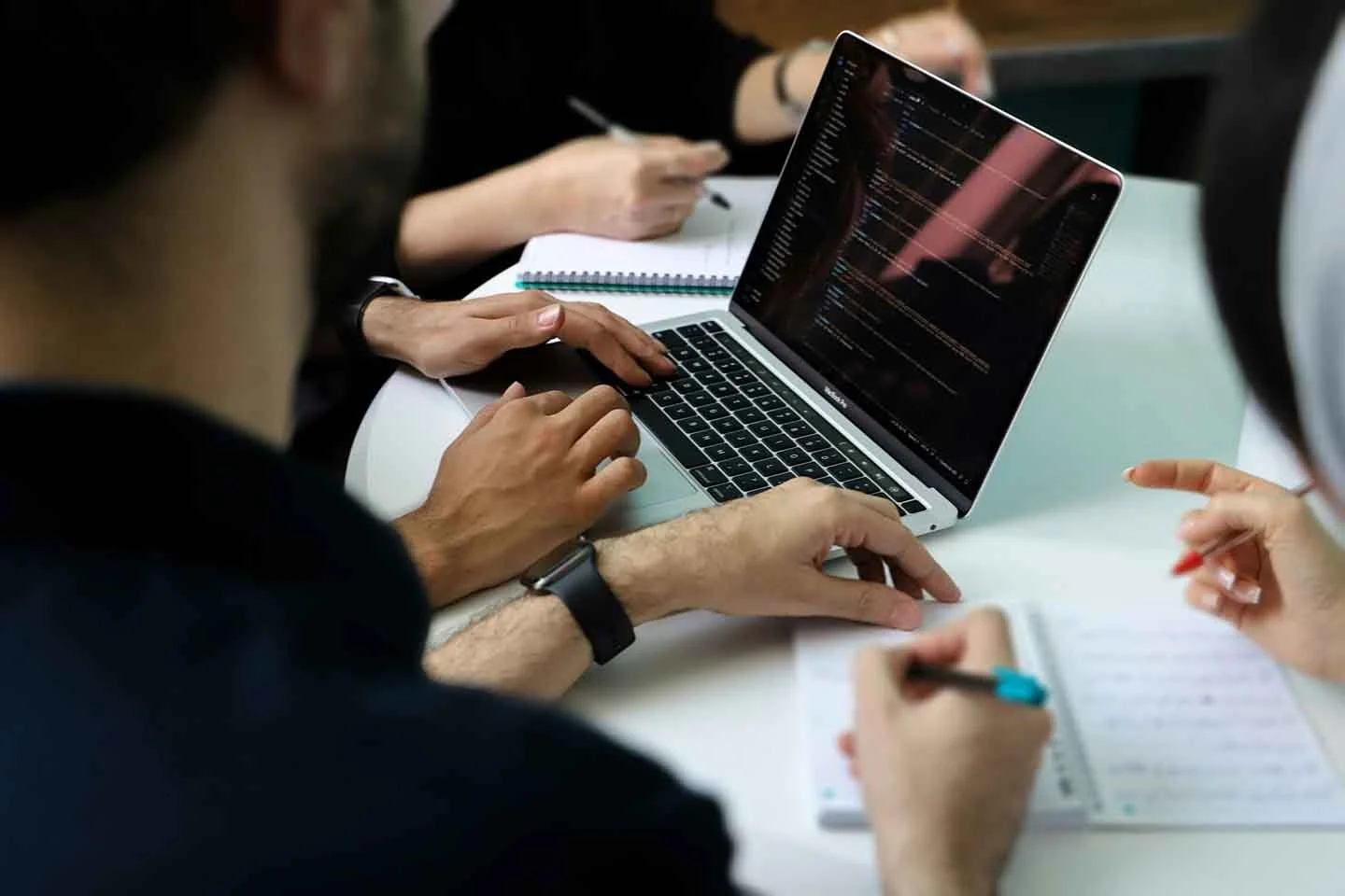 People working on a laptop displaying code at a collaborative meeting.