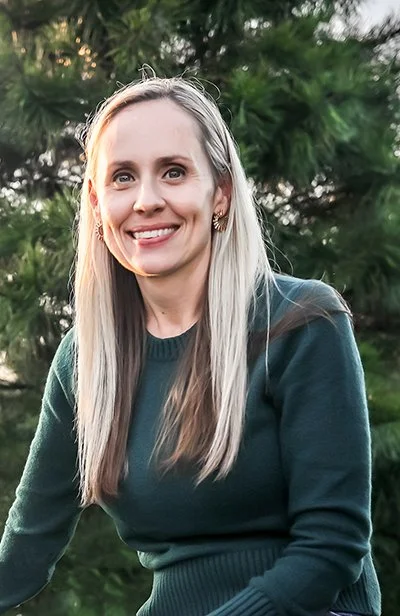 Mary Stanley in a green top standing in front of a gorgeous tree smiling.