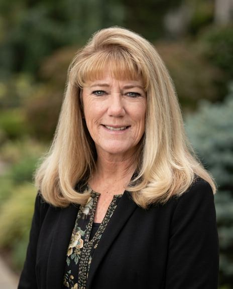 Dorene Rounds in a floral top with blazer in front of green background smiling.