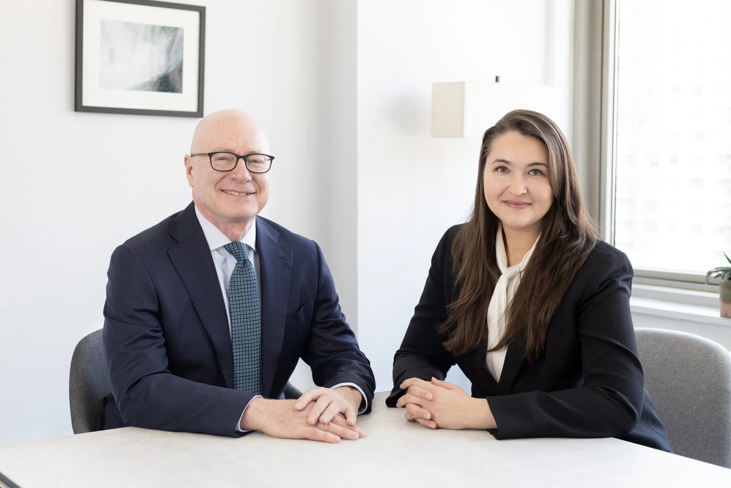 Two people in business attire sitting at a table in an office.