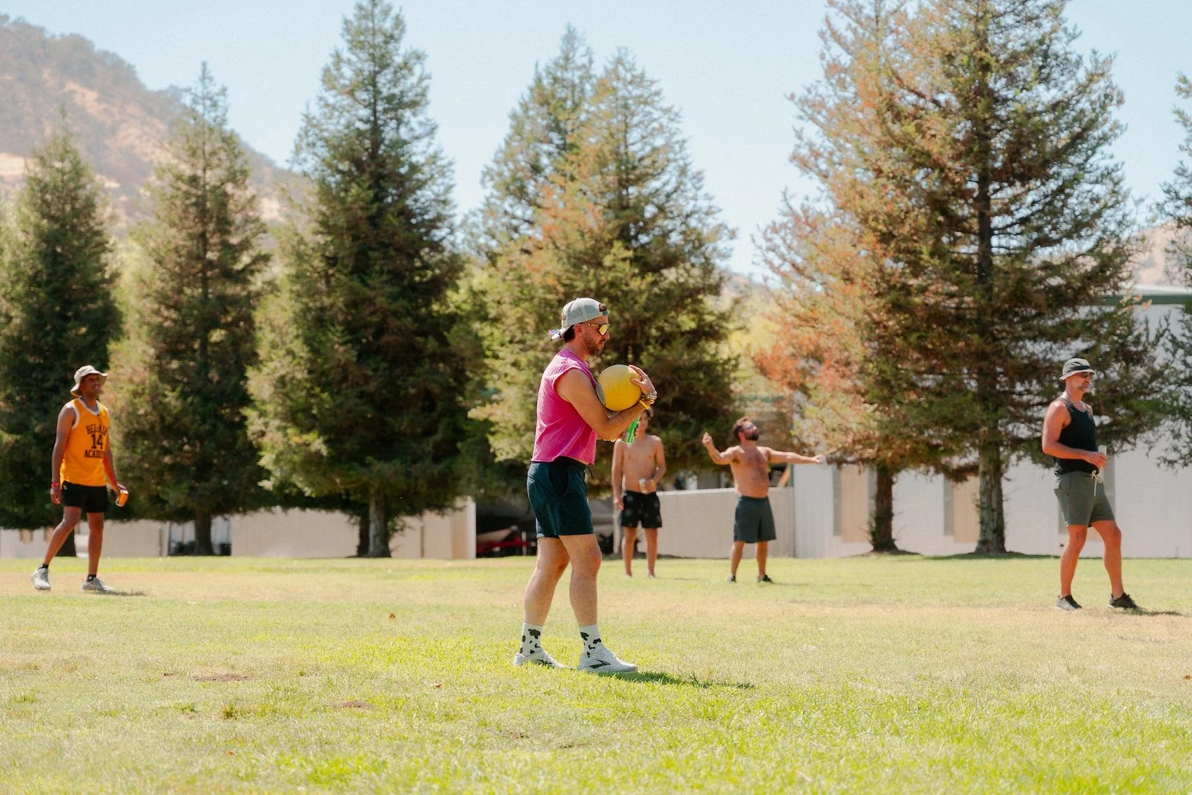 People playing recreational volleyball on a grassy field with trees and mountains in the background.