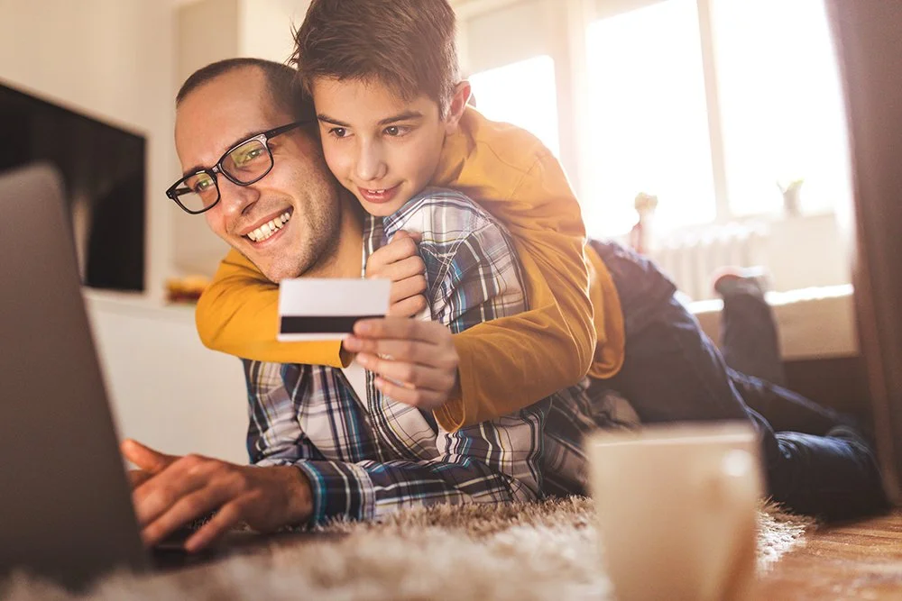 man and child using holding credit card while looking at a computer