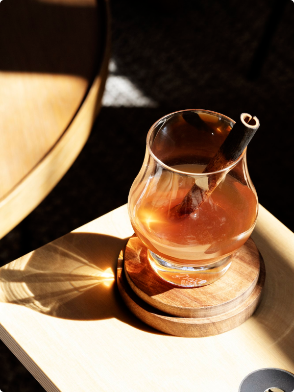 A bottle of Brother Justus Cinnamon Whiskey Liqueur, dark amber in color, on a black table at the distillery.