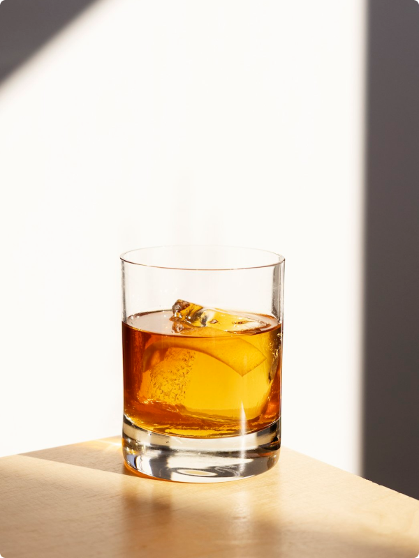 Autumn Old Fashioned, a Brother Justus cocktail, amber-hued in a rocks glass on a wooden distillery table.