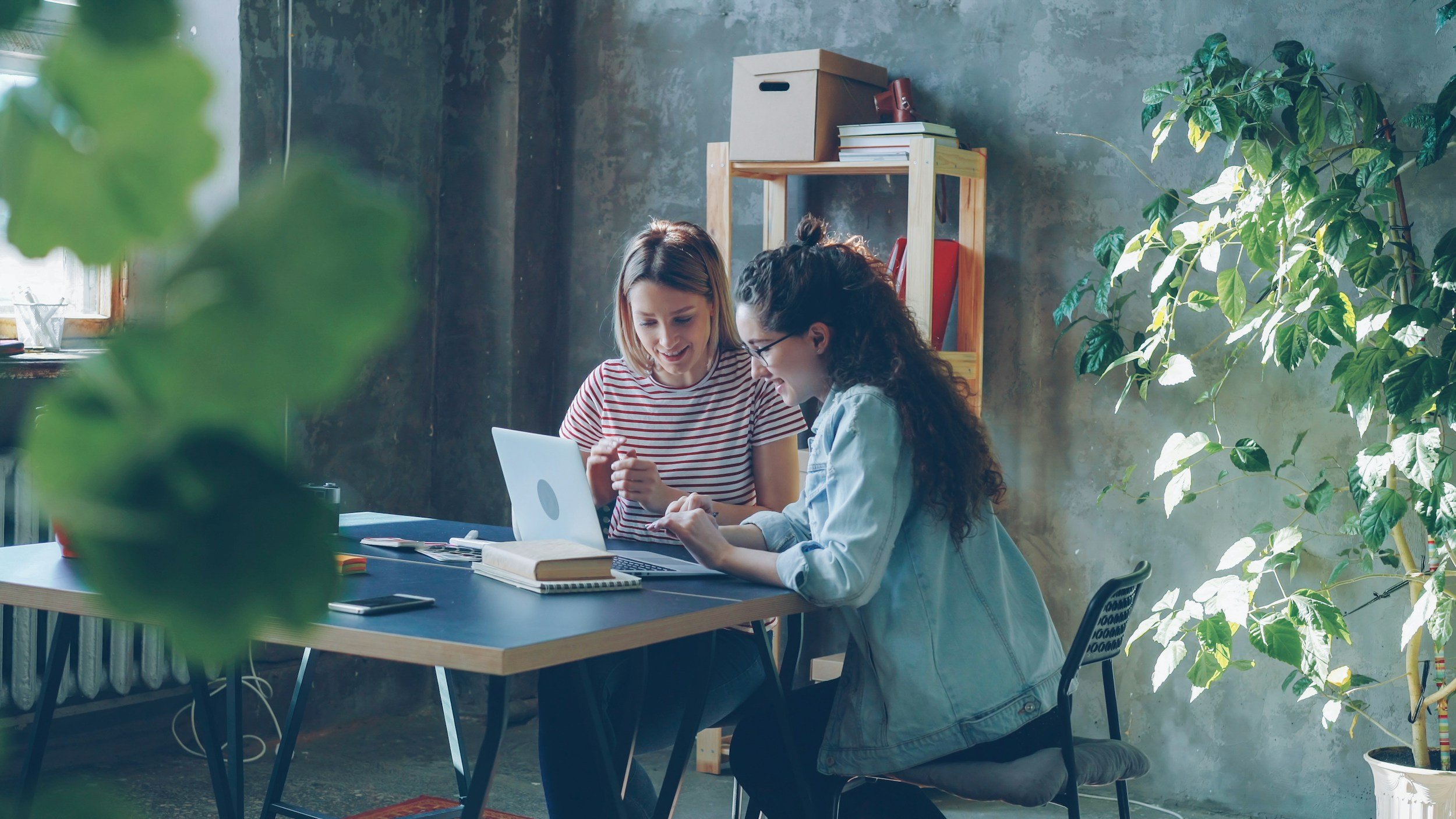 Two ladies at a desk with a computer looking happy.