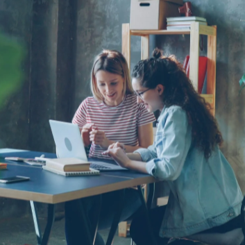 Two ladies at a desk looking at a computer with smiles.