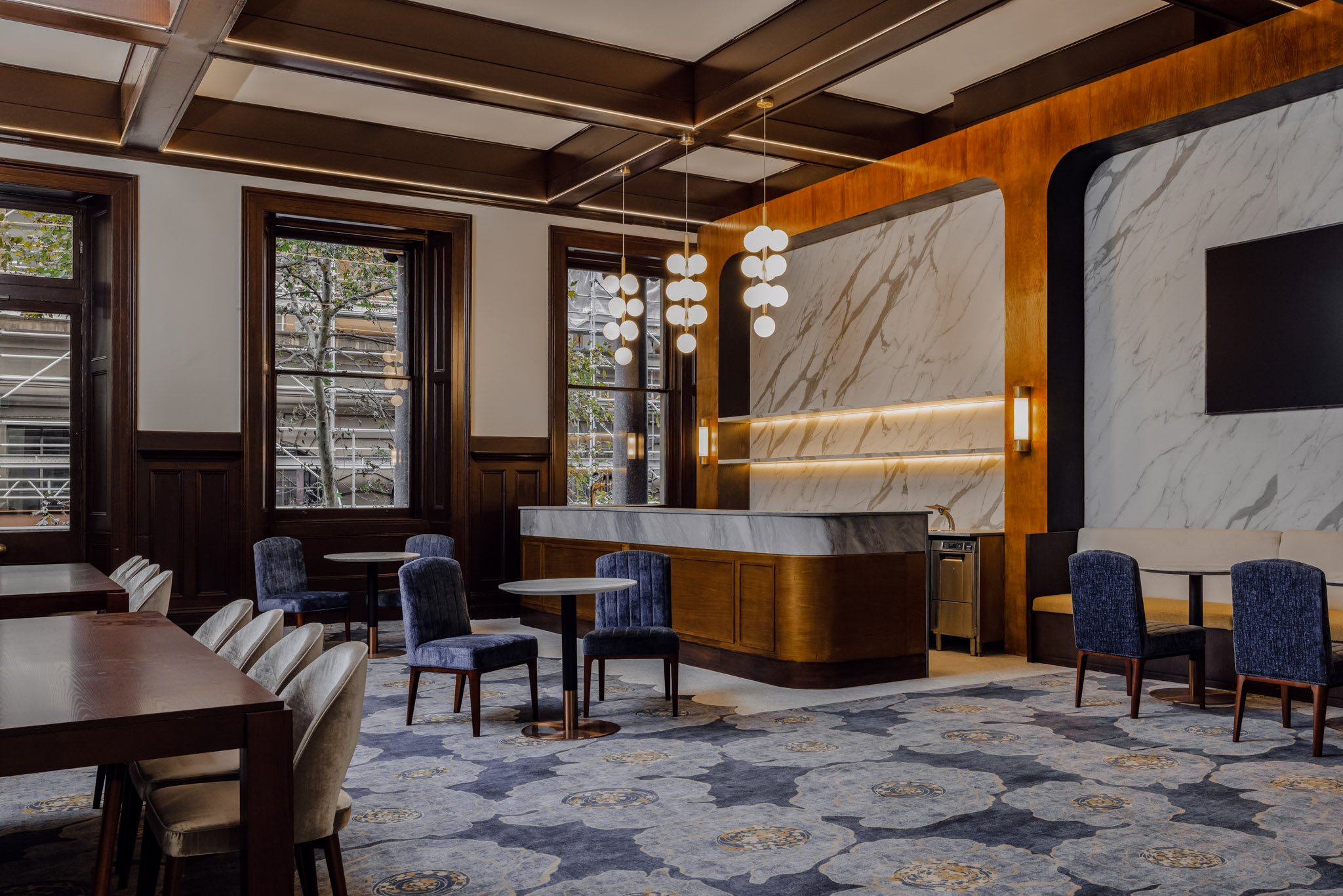Interior of a modern, upscale bar or lounge area with dark wood accents, marble walls, and stylish lighting fixtures.