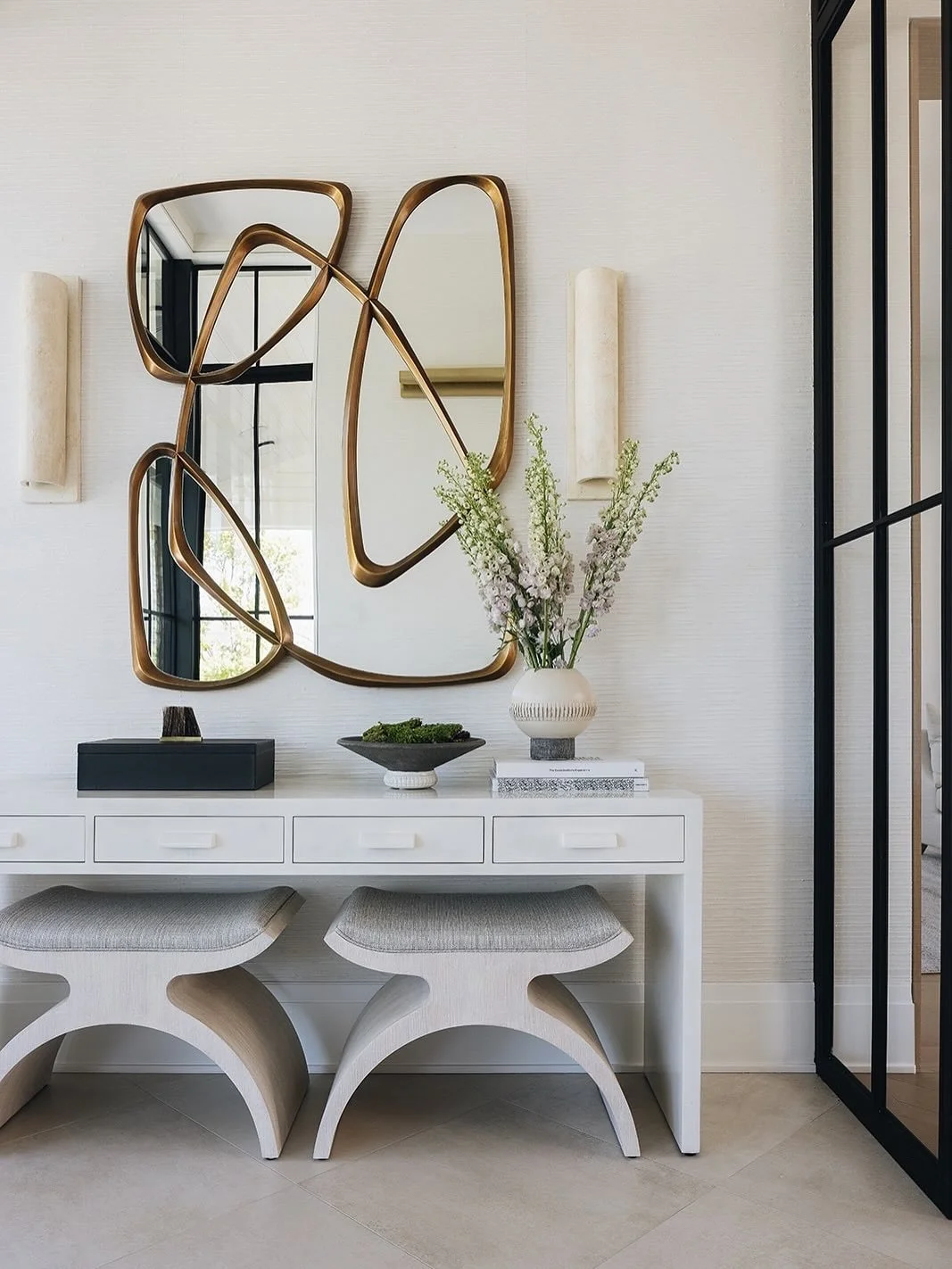 Welcome home. This curated entryway combines functionality with beauty - where every detail invites you in.
⠀⠀⠀⠀⠀⠀⠀⠀⠀
Framed by custom metal and glass doors, the foyer becomes a defined moment within the home. A sculptural mirror with organic lines i